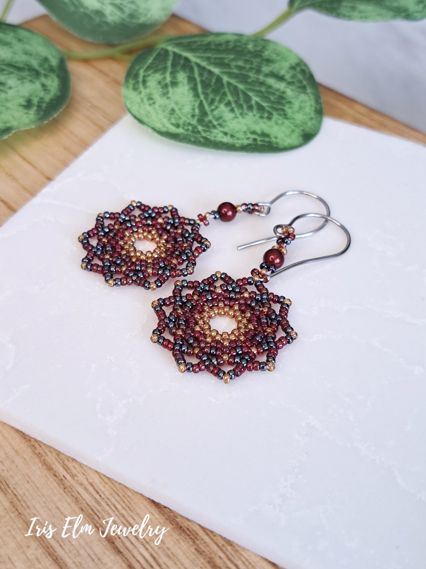 Beaded red mandala earrings on a white stone with green leaves in the background