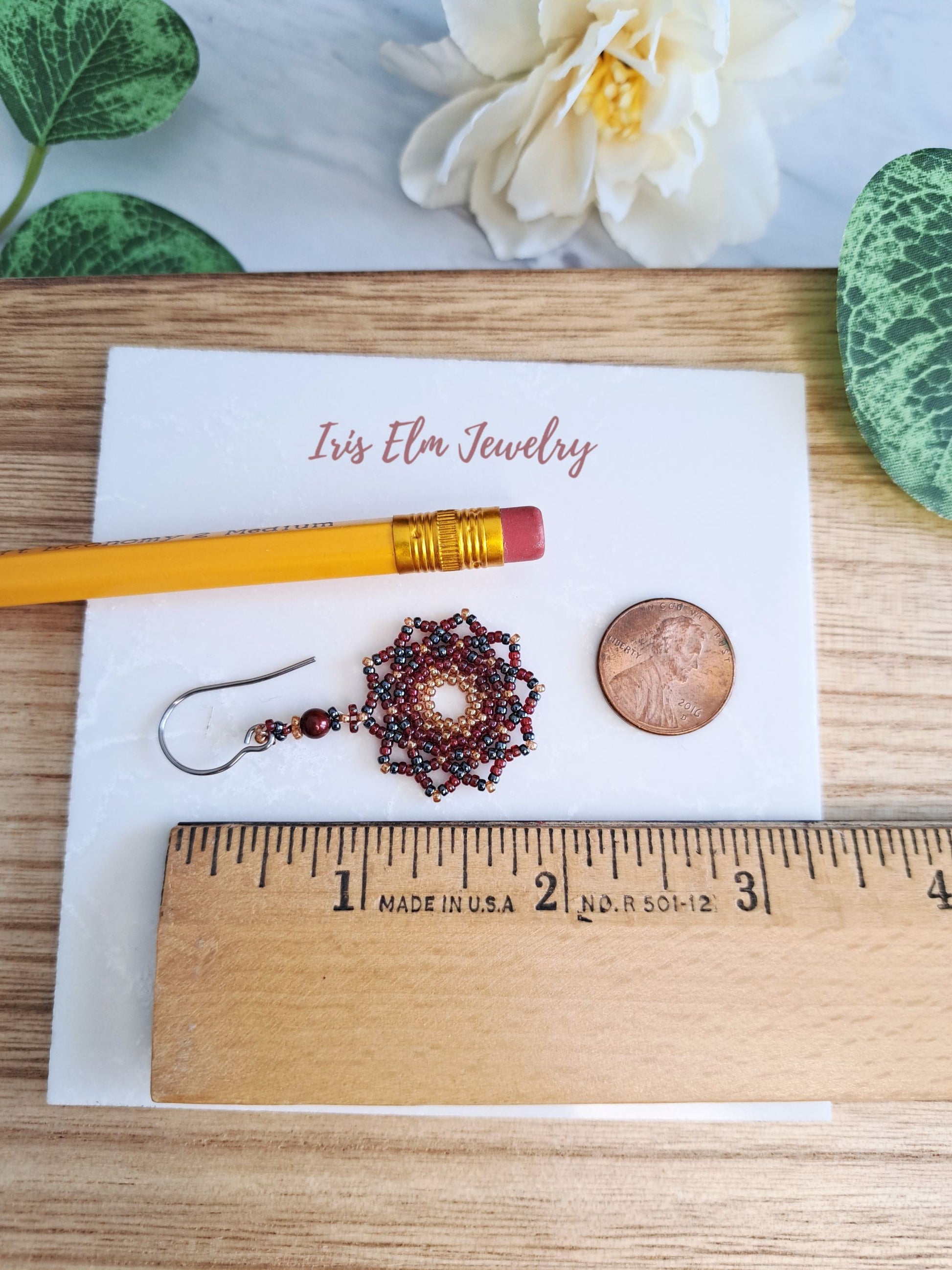 1 and 7/8 inch long red mandala earring displayed on a card with a pencil and coin for scale, on a wooden surface.