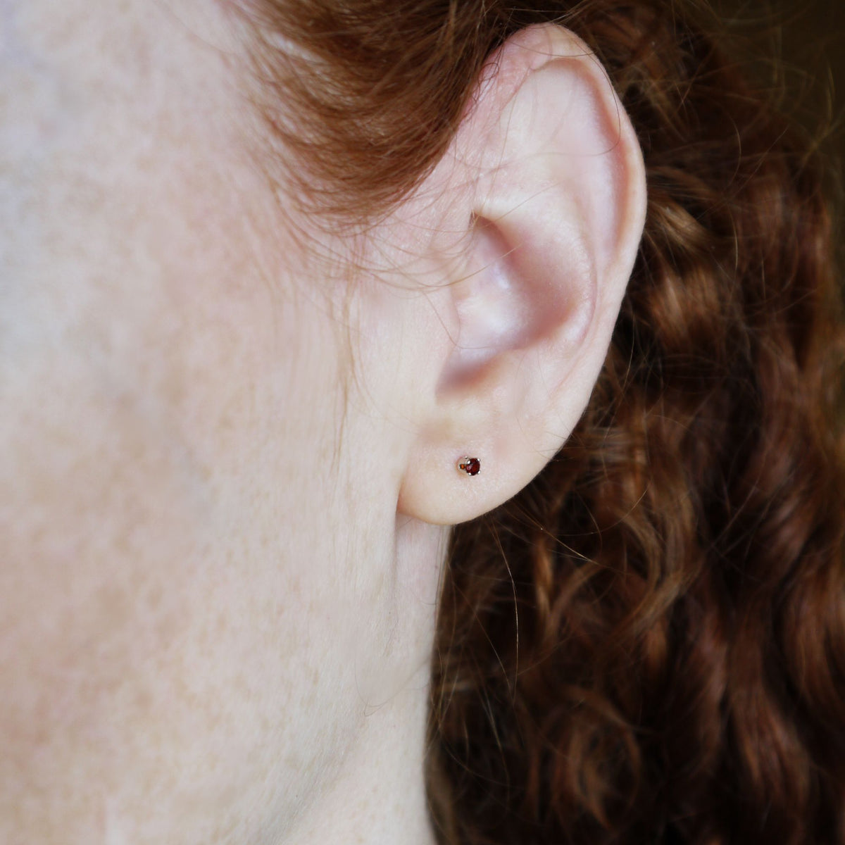 Close-up of an ear with a small garnet stud earring, hair partially covering the frame