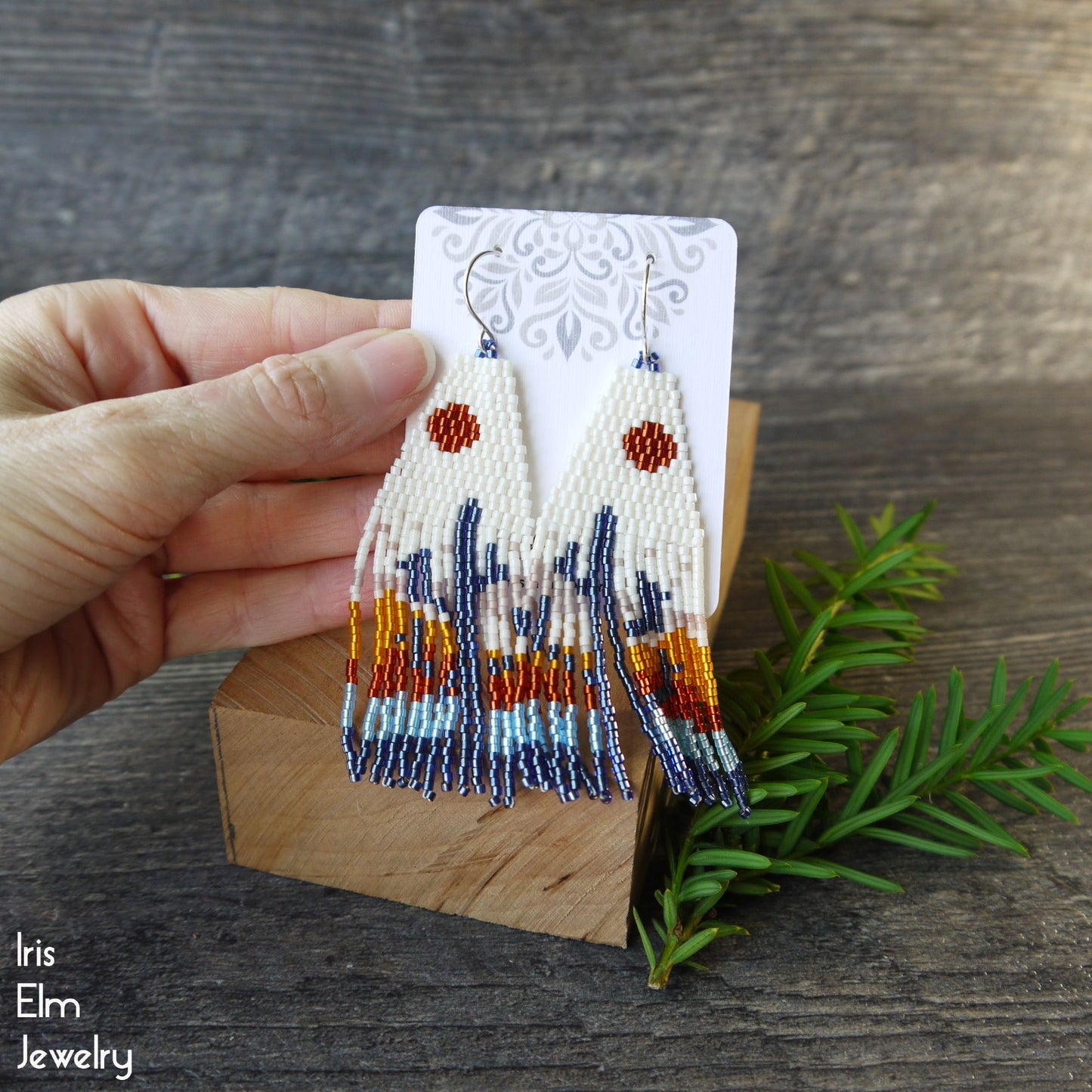 Hand holding a pair of beaded cactus earrings on a wooden stand with a natural background