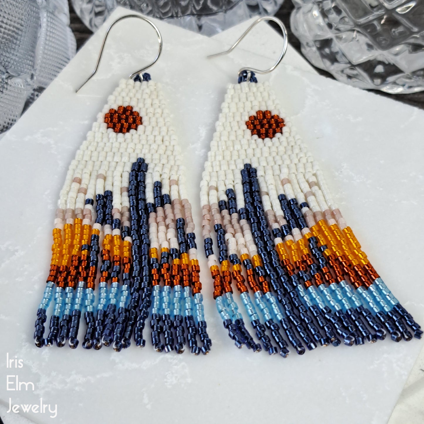 Beaded glass fringe earrings with colorful pattern on a white surface, branded 'Iris Elm Jewelry'.