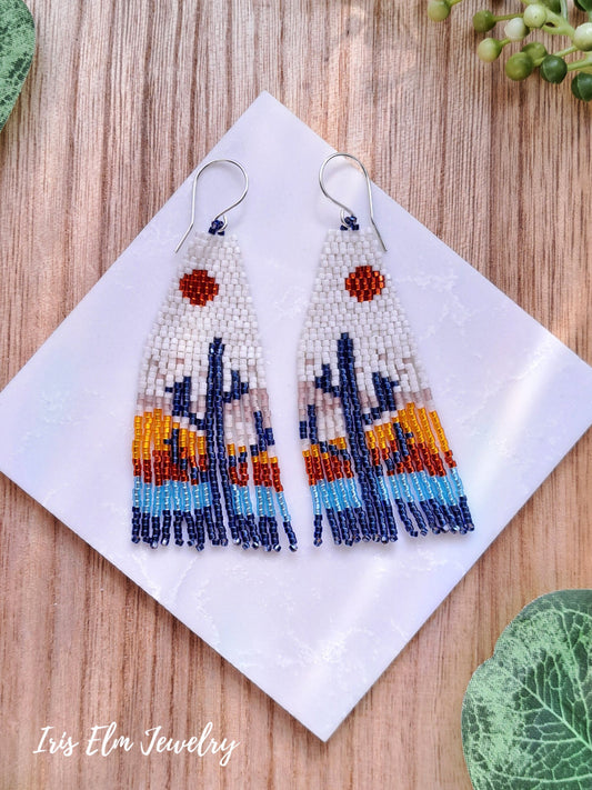Beaded desert sunset cactus seed bead fringe earrings on a white square with 'Iris Elm Jewelry' branding, placed on a wooden surface.