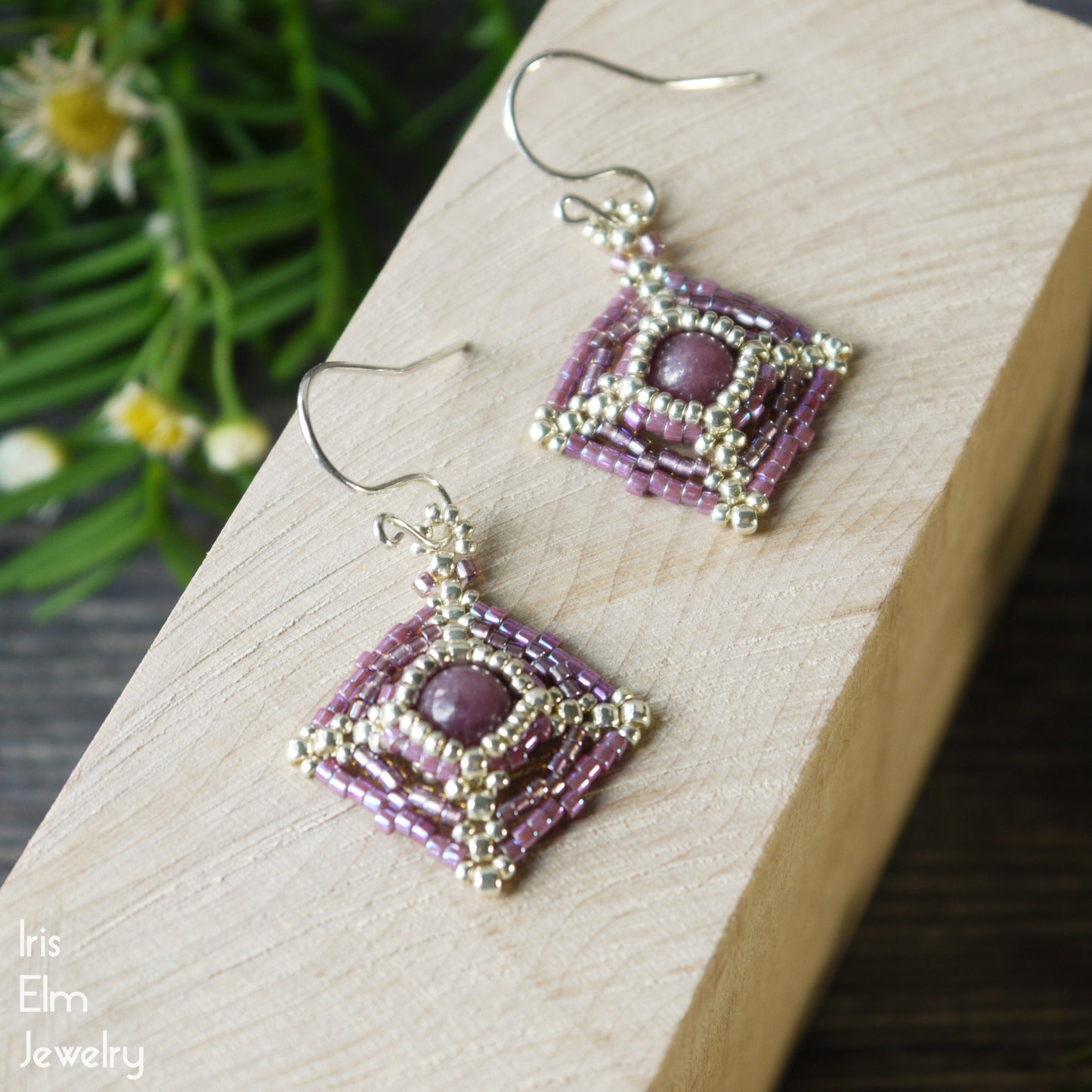 Pair of beaded pink-purple and silver lepidolite woven earrings on a wooden surface with a natural background