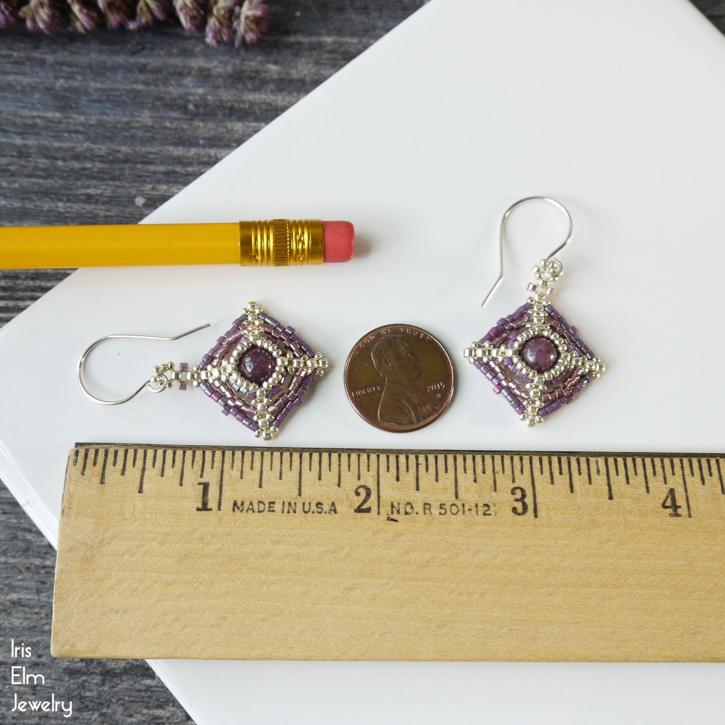 Pair of 1 and 5/8 inch long purple beaded earrings on a white surface with a penny and pencil for scale, featuring 'Iris Elm Jewelry' branding.