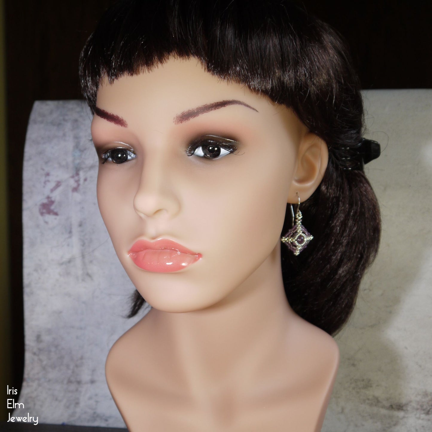 Mannequin head with dark hair and a lepidolite earring on a neutral background