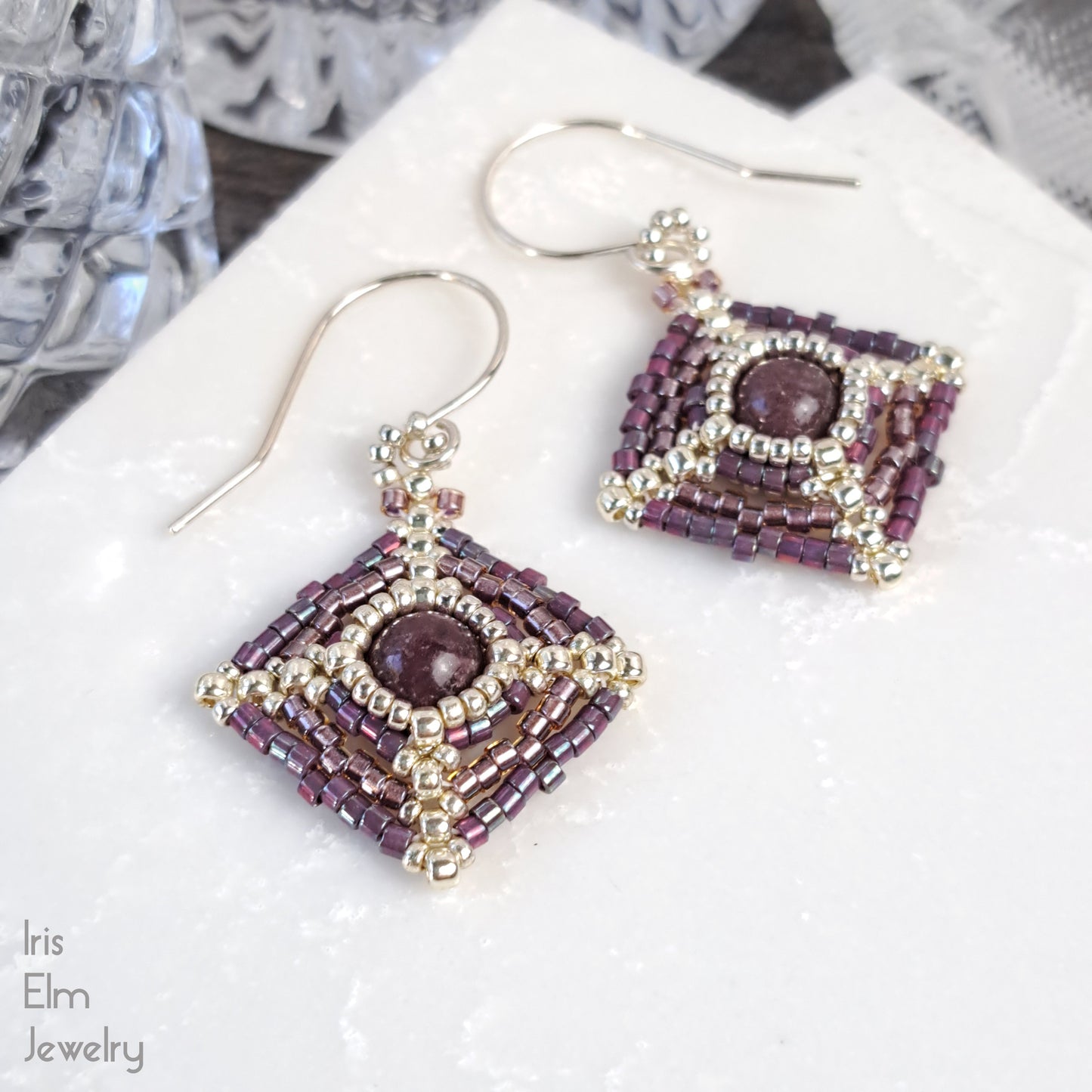 Pair of beaded lepidolite stone and seed bead earrings on a white surface with 'Iris Elm Jewelry' branding.