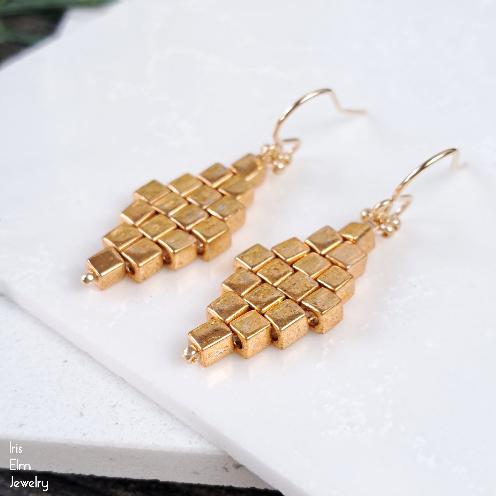 Gold geometric beadwork earrings with gold filled ear wires on a white surface with 'Iris Elm Jewelry' branding.