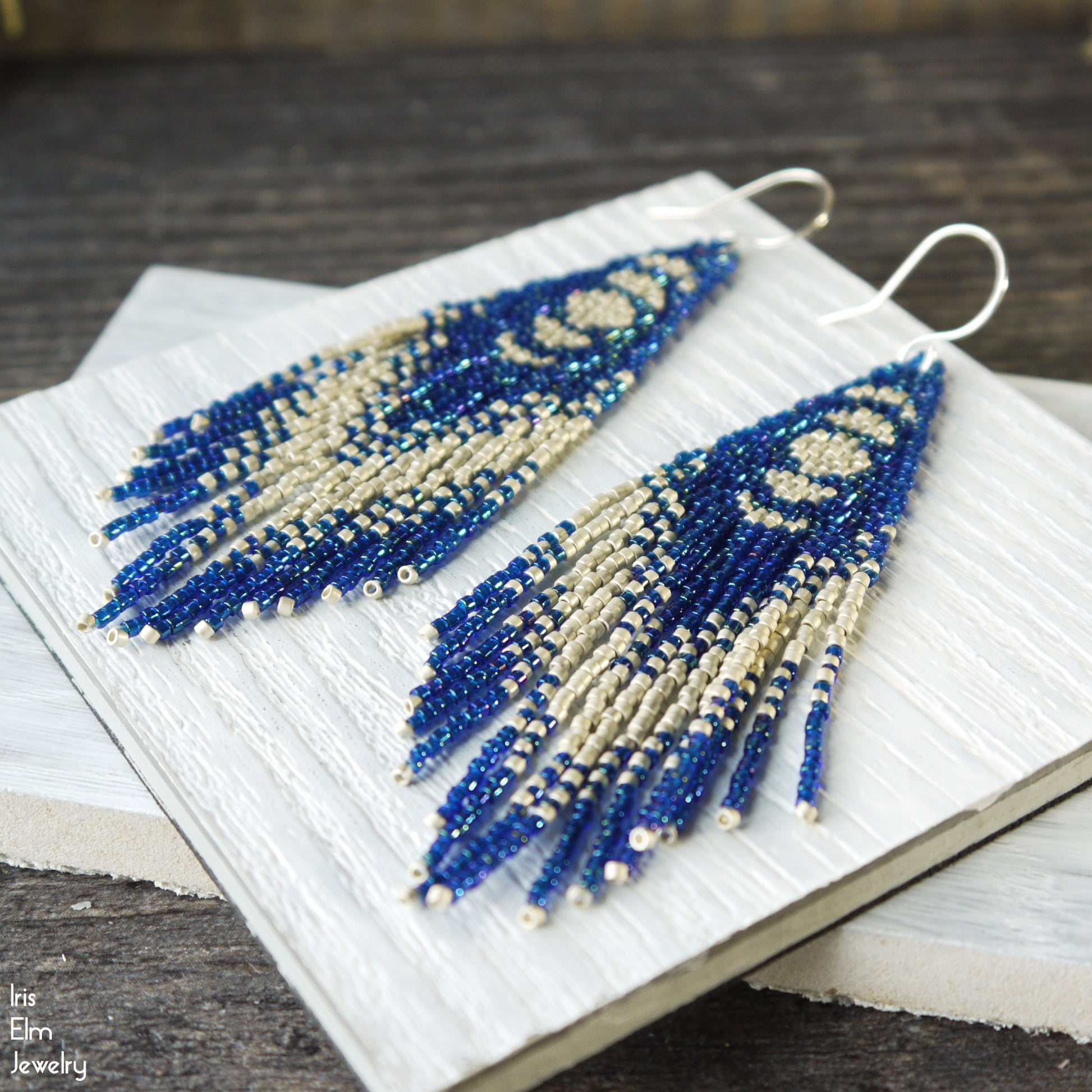 Blue moon phase seed bead fringe glass earrings on a white fabric background
