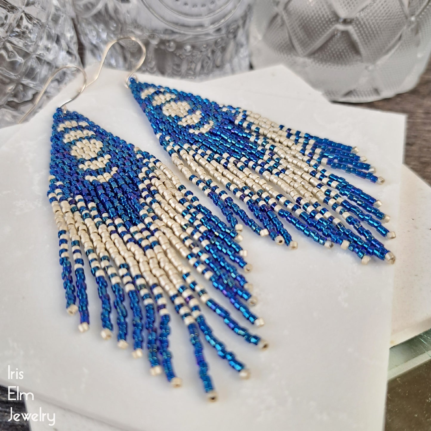 Blue and light grey beaded long seed bead fringe earrings with moon phase design on a white surface with 'Iris Elm Jewelry' branding.