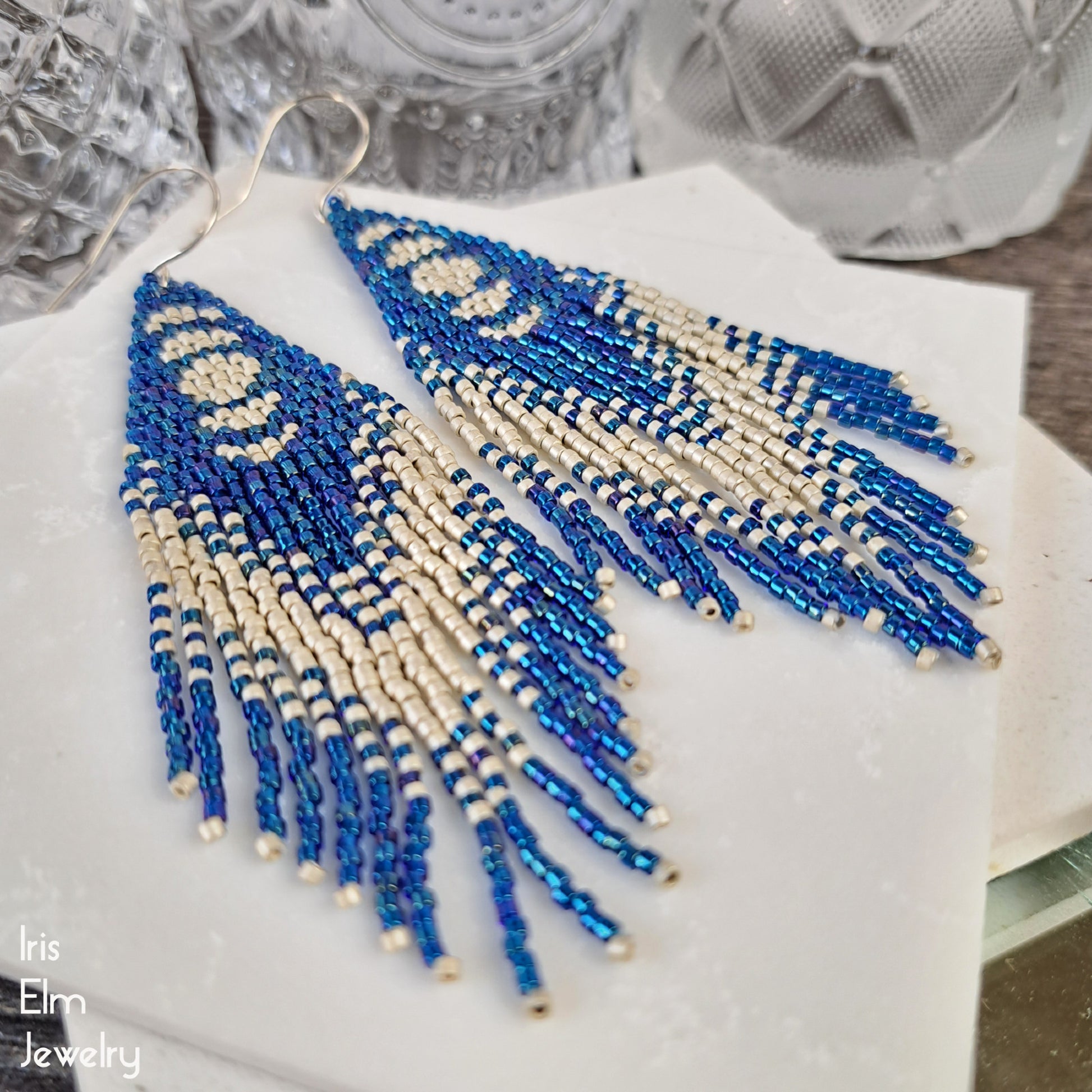 Blue and light grey beaded long seed bead fringe earrings with moon phase design on a white surface with 'Iris Elm Jewelry' branding.