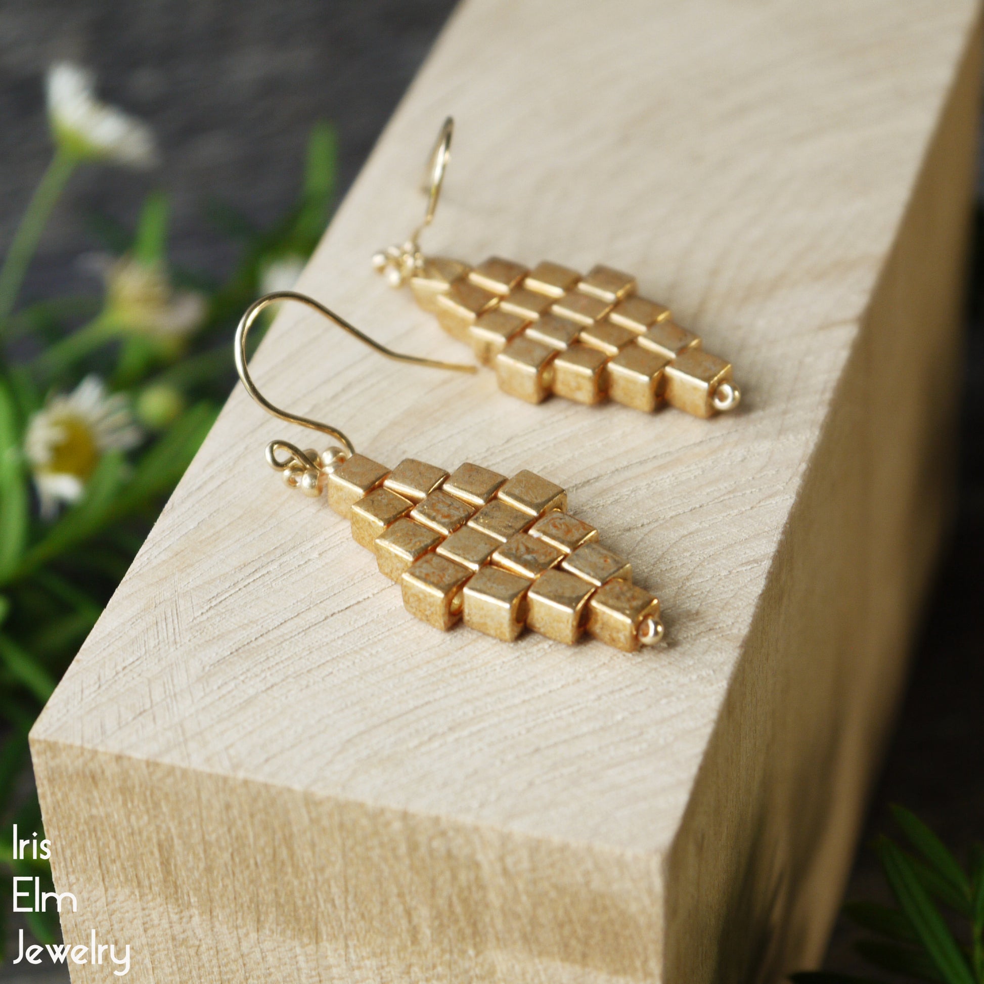 Gold geometric earrings with cube beads on a wooden block with a natural background