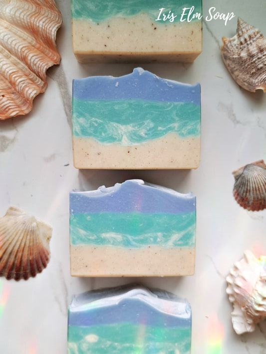 Three layered coconut lime verbena handmade soap bars with ocean design surrounded by seashells on a marble surface