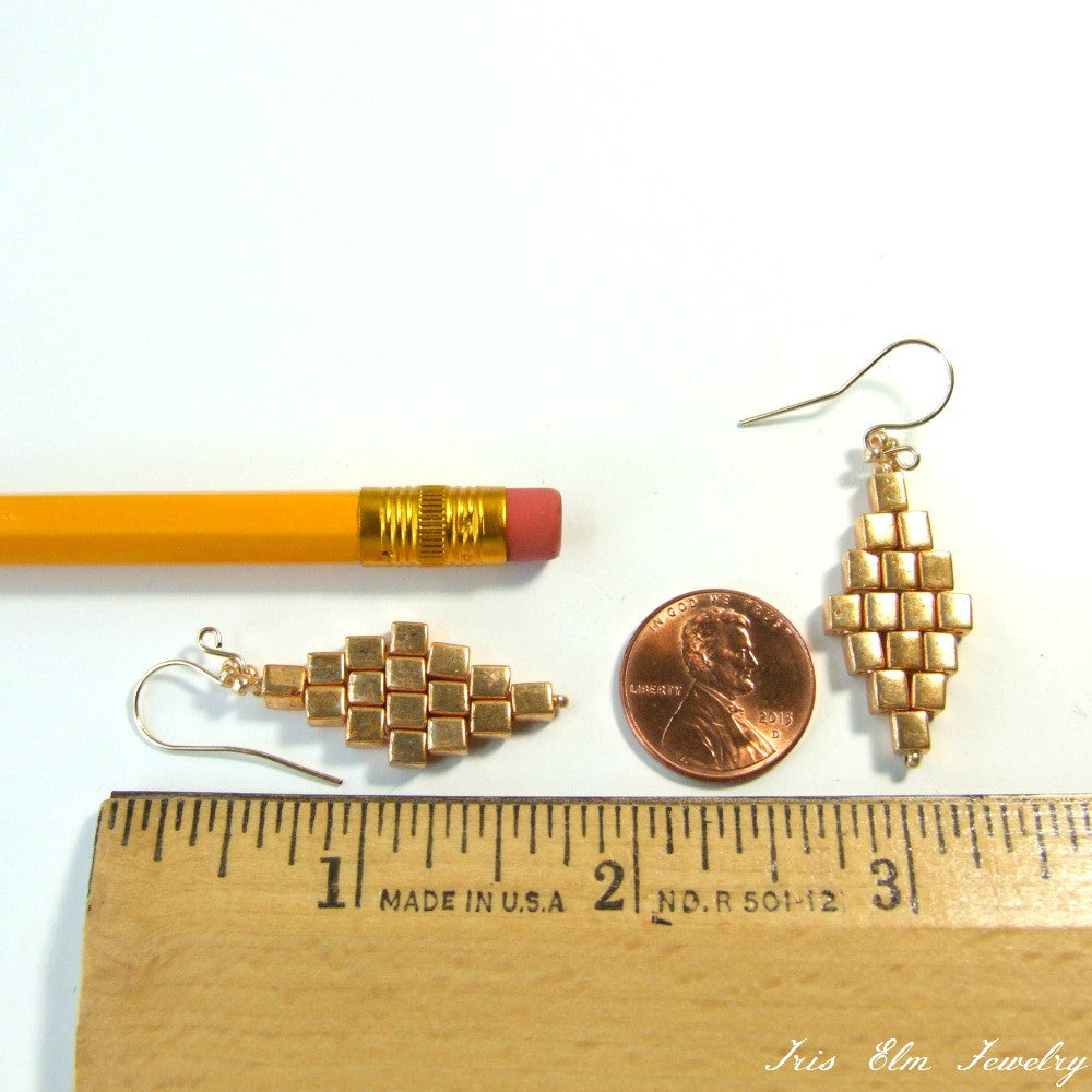Gold earrings with a ruler for scale on a white background