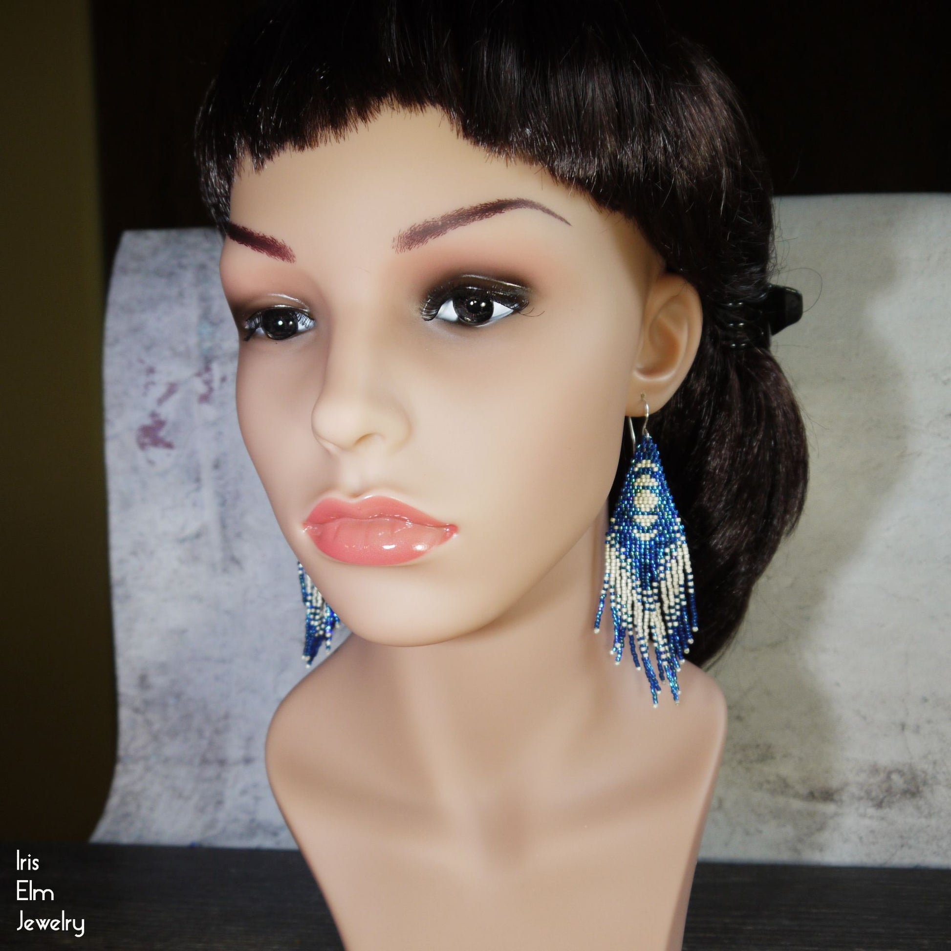 Mannequin head with blue beaded moon phase fringe earrings on a neutral background