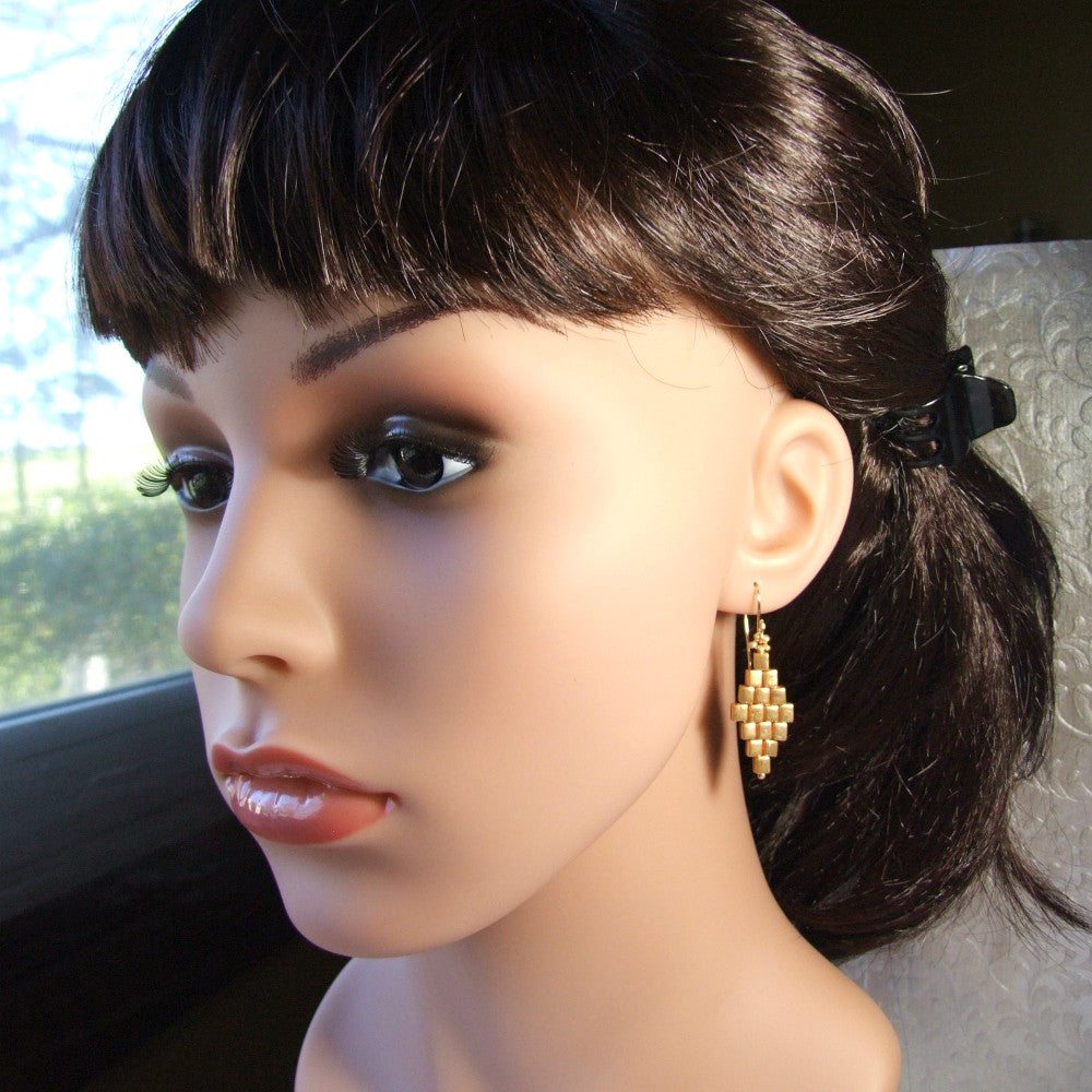 Mannequin head with dark hair styled in a ponytail and wearing gold diamond shape earrings.