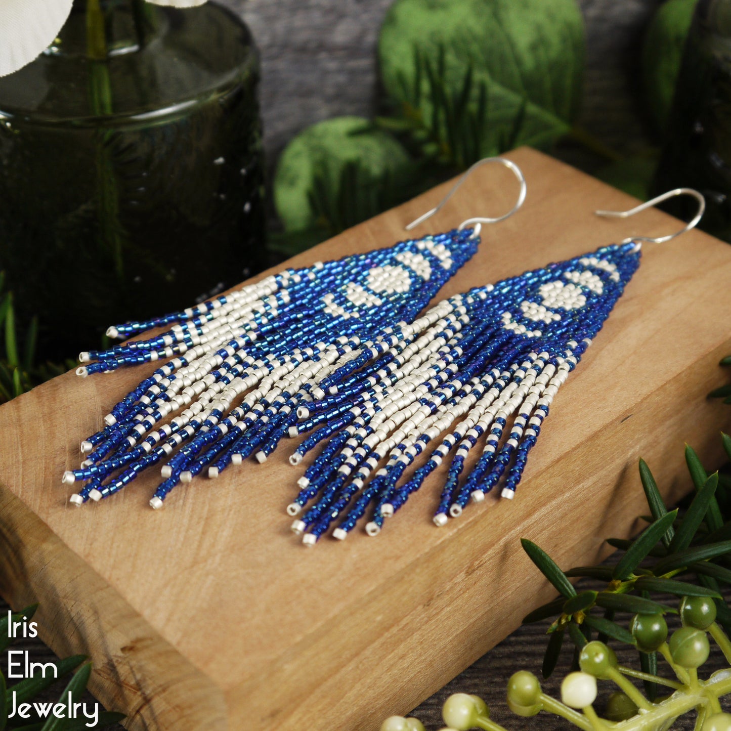 Blue and white beaded long fringe celestial moon earrings on a wooden surface with 'Iris Elm Jewelry' branding.