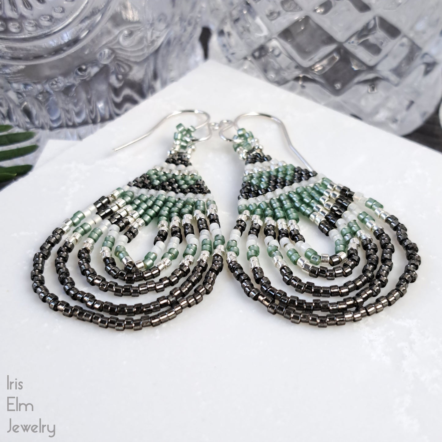 Beaded handmade green glass teardrop earrings on a white surface with 'Iris Elm Jewelry' branding.