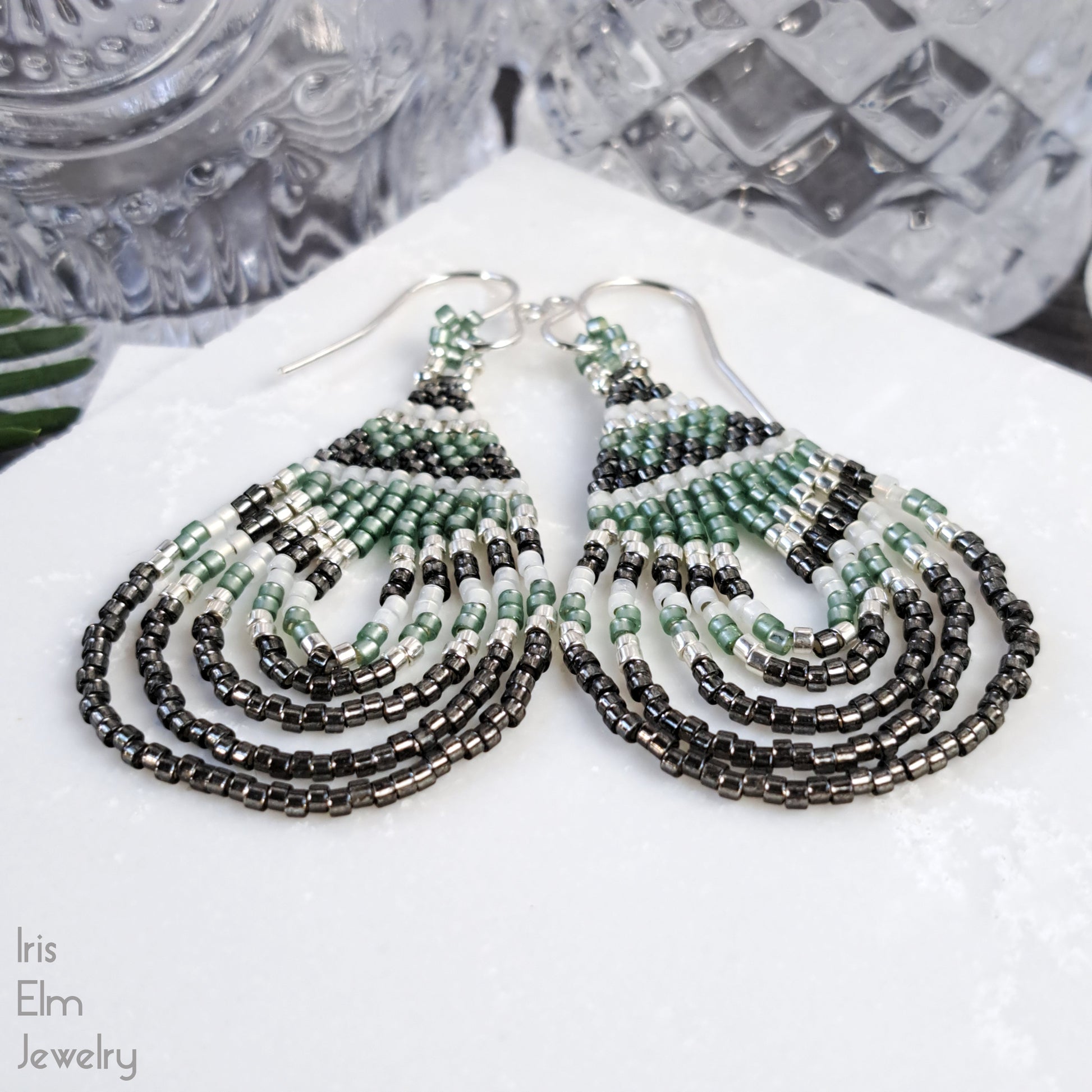 Beaded handmade green glass teardrop earrings on a white surface with 'Iris Elm Jewelry' branding.