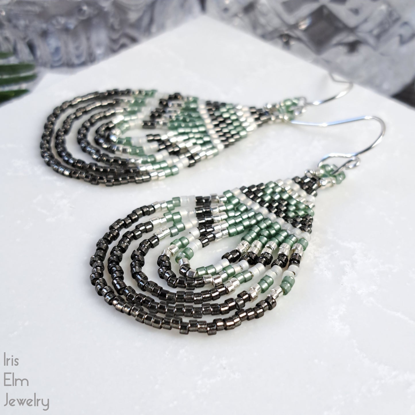 Beaded teardrop green and grey seed bead earrings on a white surface with 'Iris Elm Jewelry' branding.