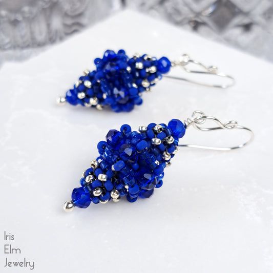 Blue beaded glass earrings with sterling silver ear wires on a white surface with 'Iris Elm Jewelry' branding.