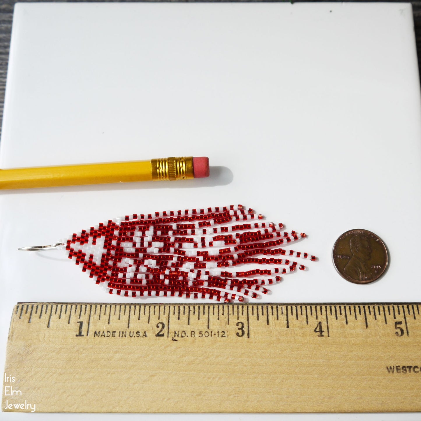 4 inch long red and white beaded fringe earrings with a pencil and coin for scale on a white background