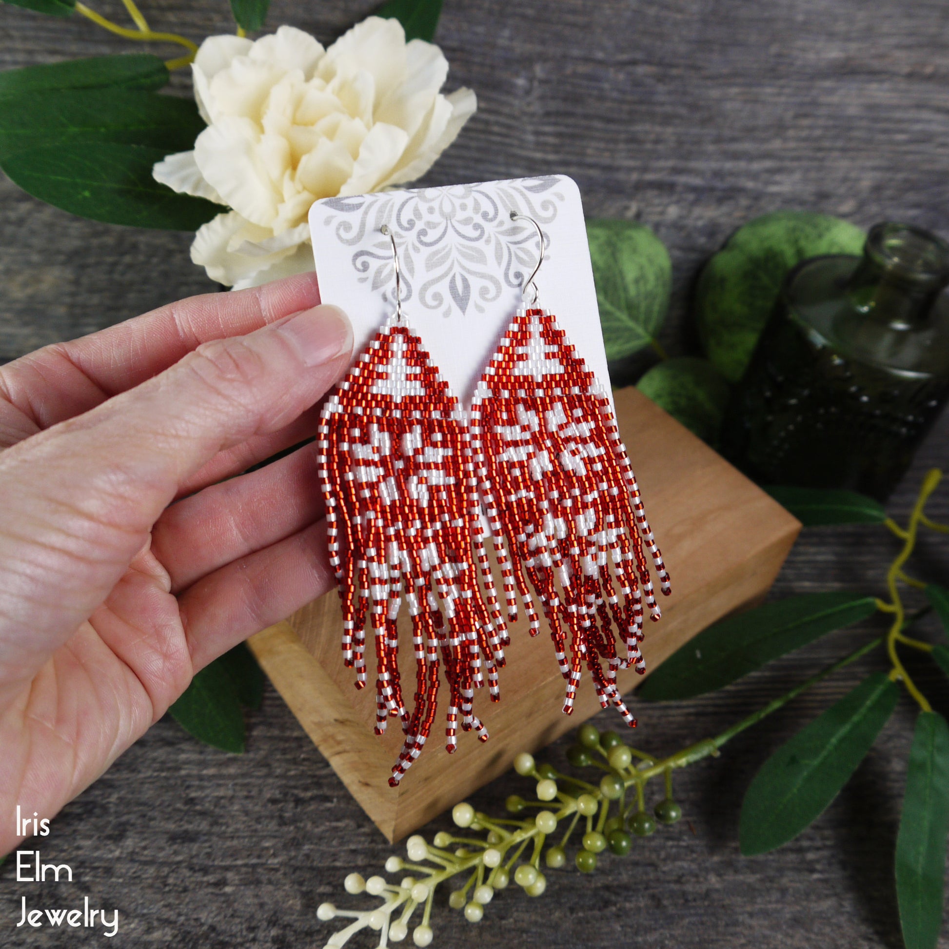 Red beaded winter fringe christmas earrings held by a hand with a floral background