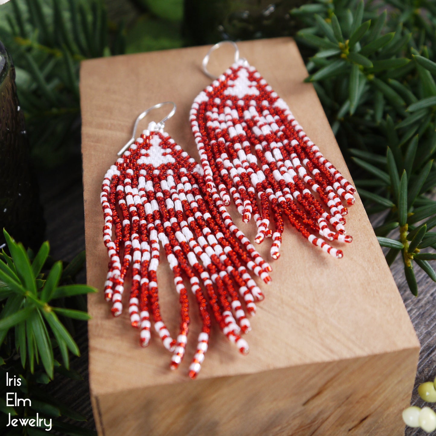Red and white beaded earrings on a wooden block with greenery in the background