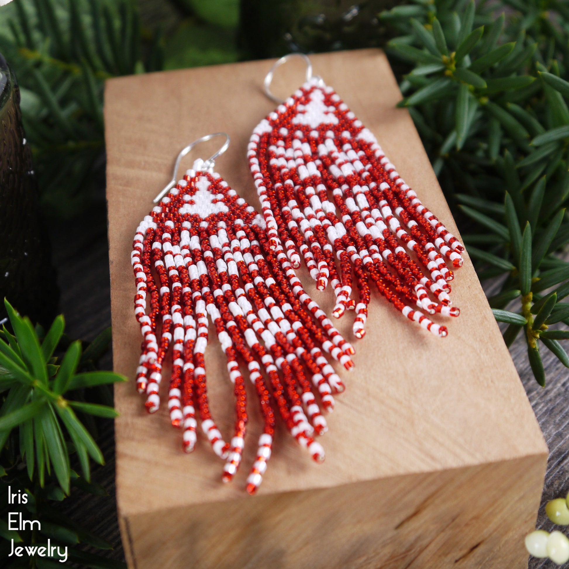 Red and white beaded earrings on a wooden block with greenery in the background