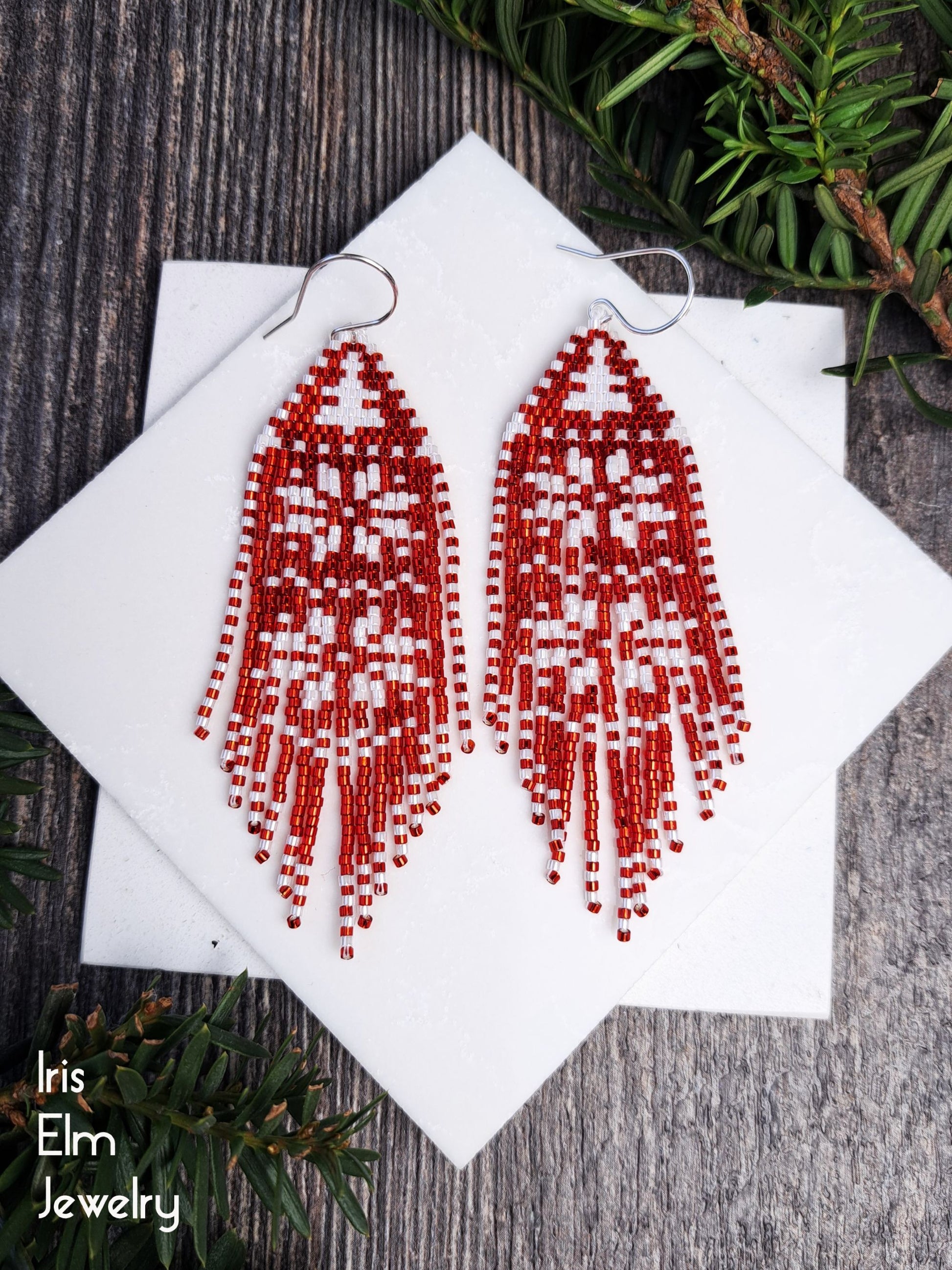 Red beaded earrings on a white card with a wooden background