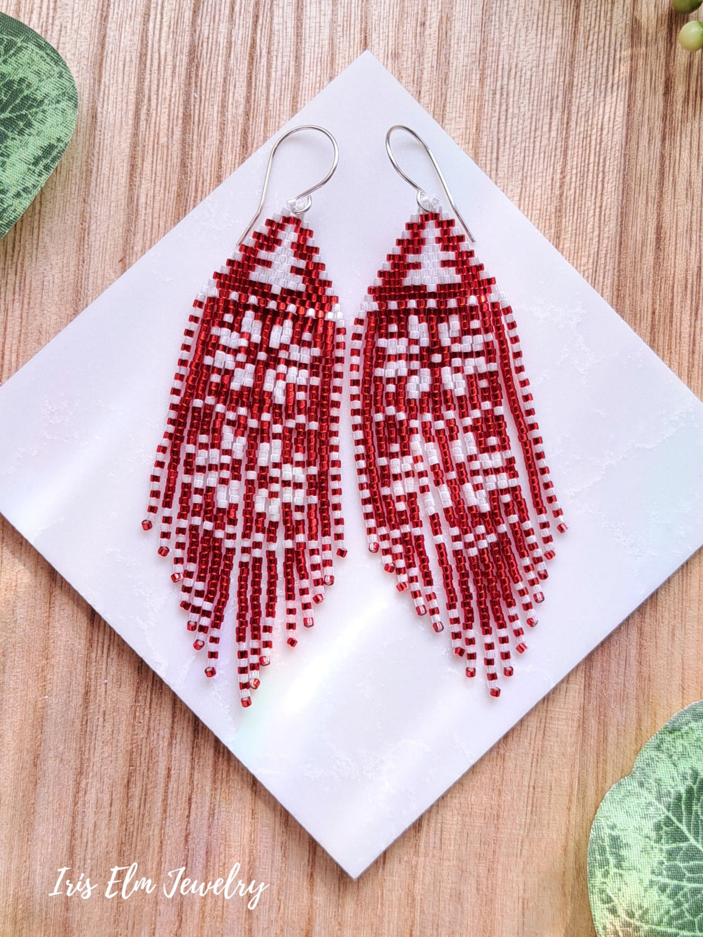 Red and white snowflake fringe beaded earrings on a white cloth with 'Iris Elm Jewelry' branding.