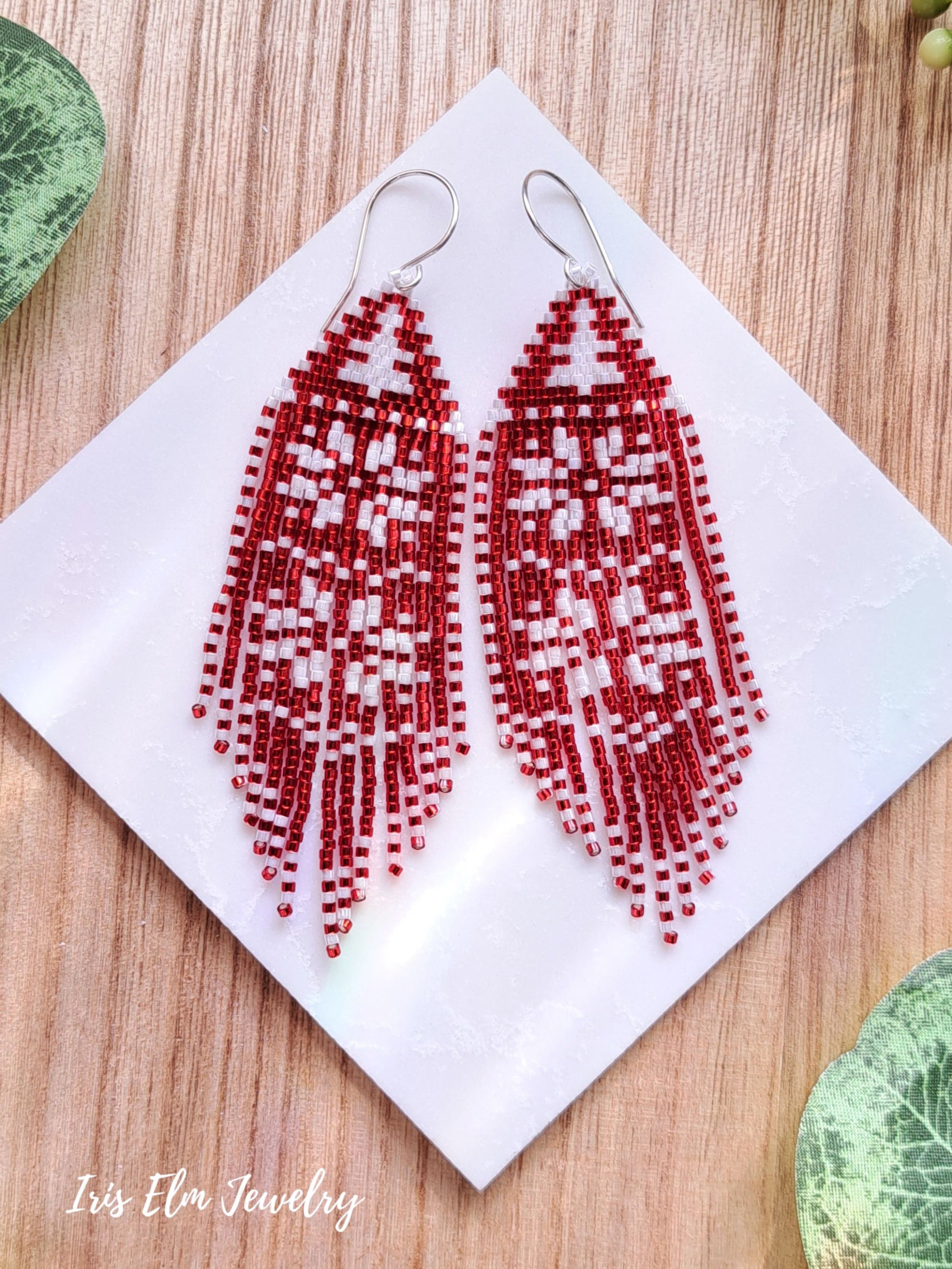 Red and white snowflake fringe beaded earrings on a white cloth with 'Iris Elm Jewelry' branding.