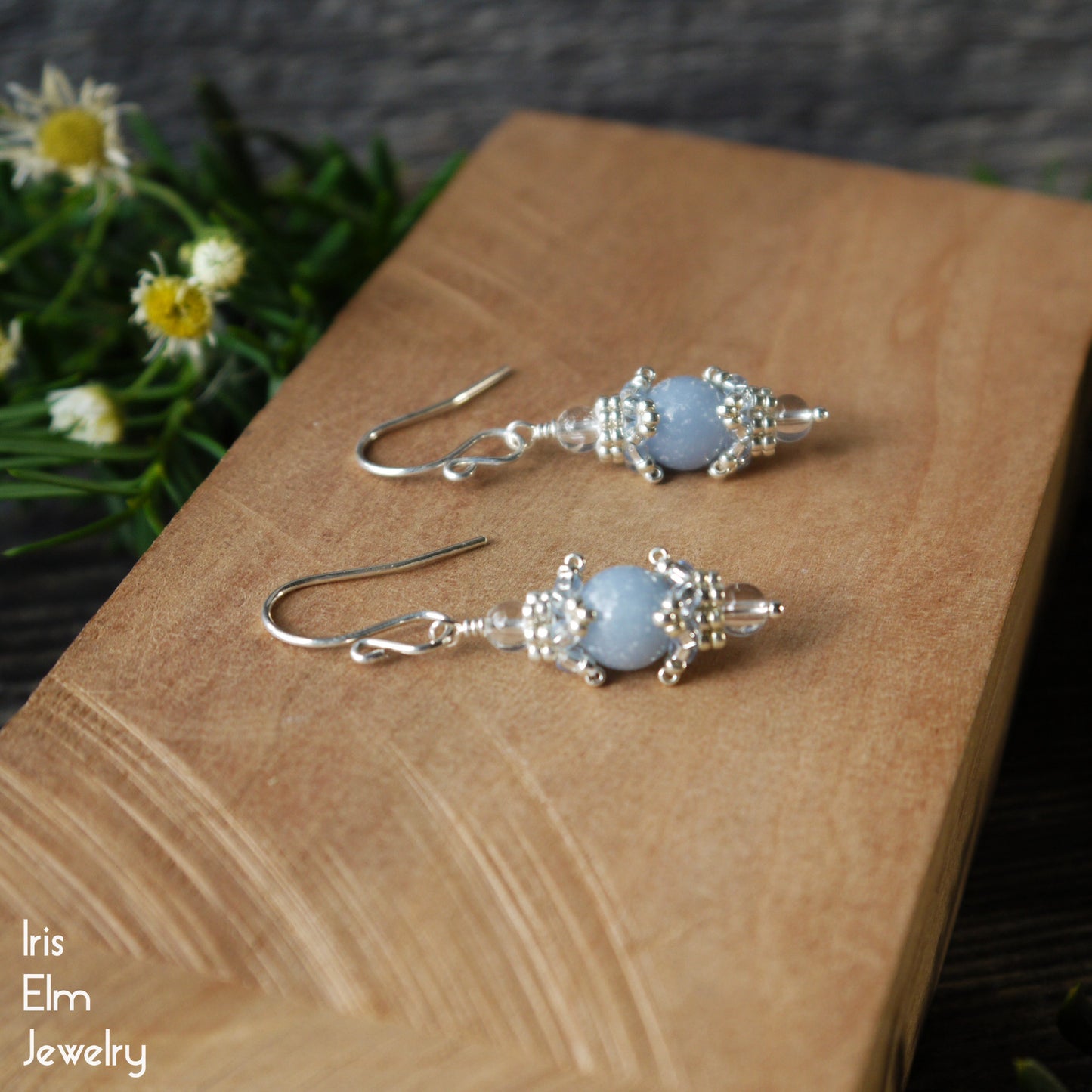 Pair of sterling silver earrings with angelite blue stones on a wooden surface, with 'Iris Elm Jewelry' branding.