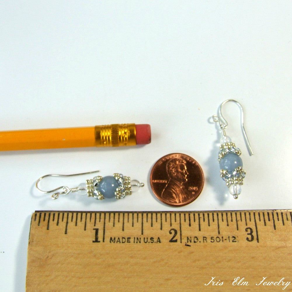 Pair of earrings with blue stones next to a pencil, penny, and ruler for scale on a white background.