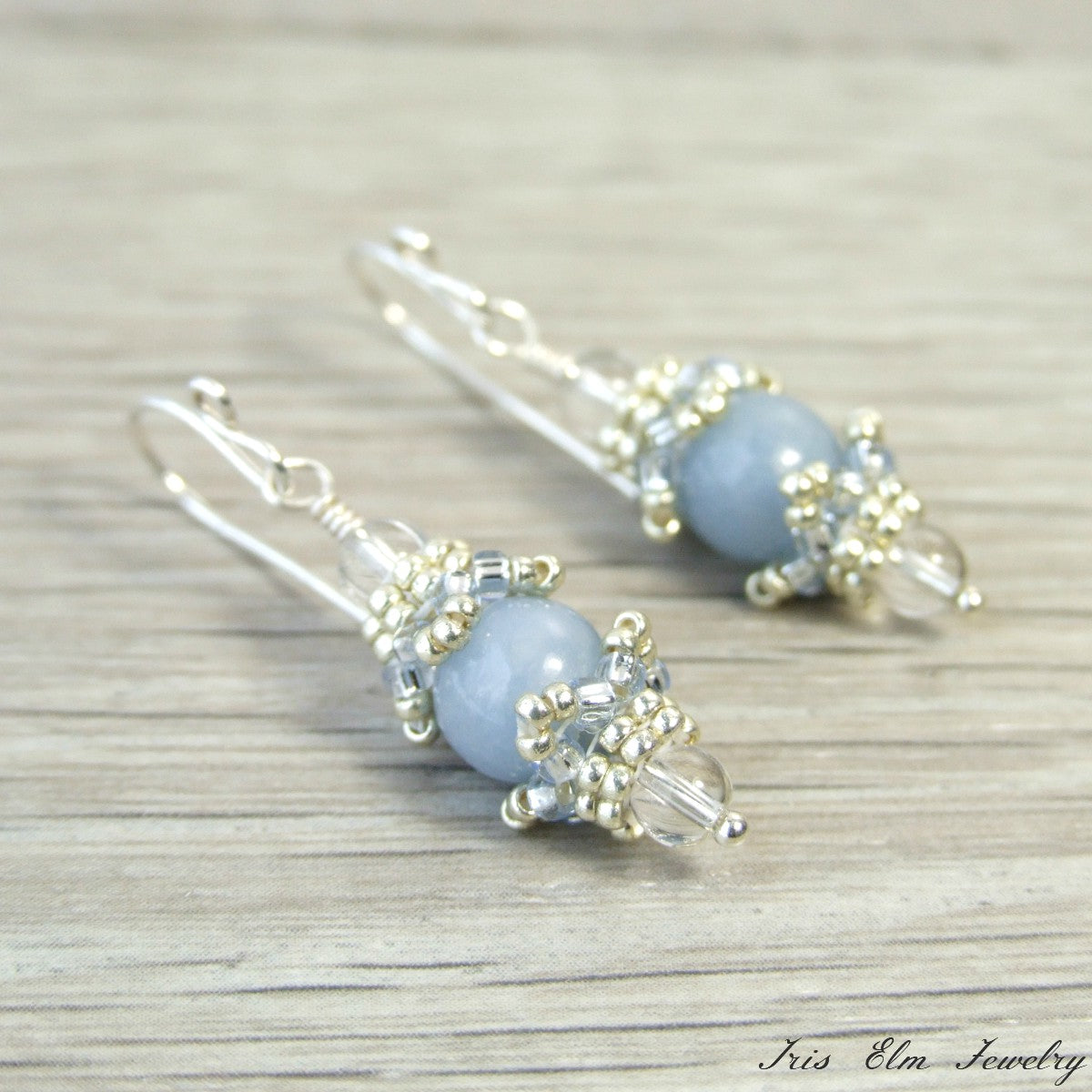 Pair of light blue beaded earrings with silver accents on a wooden surface.