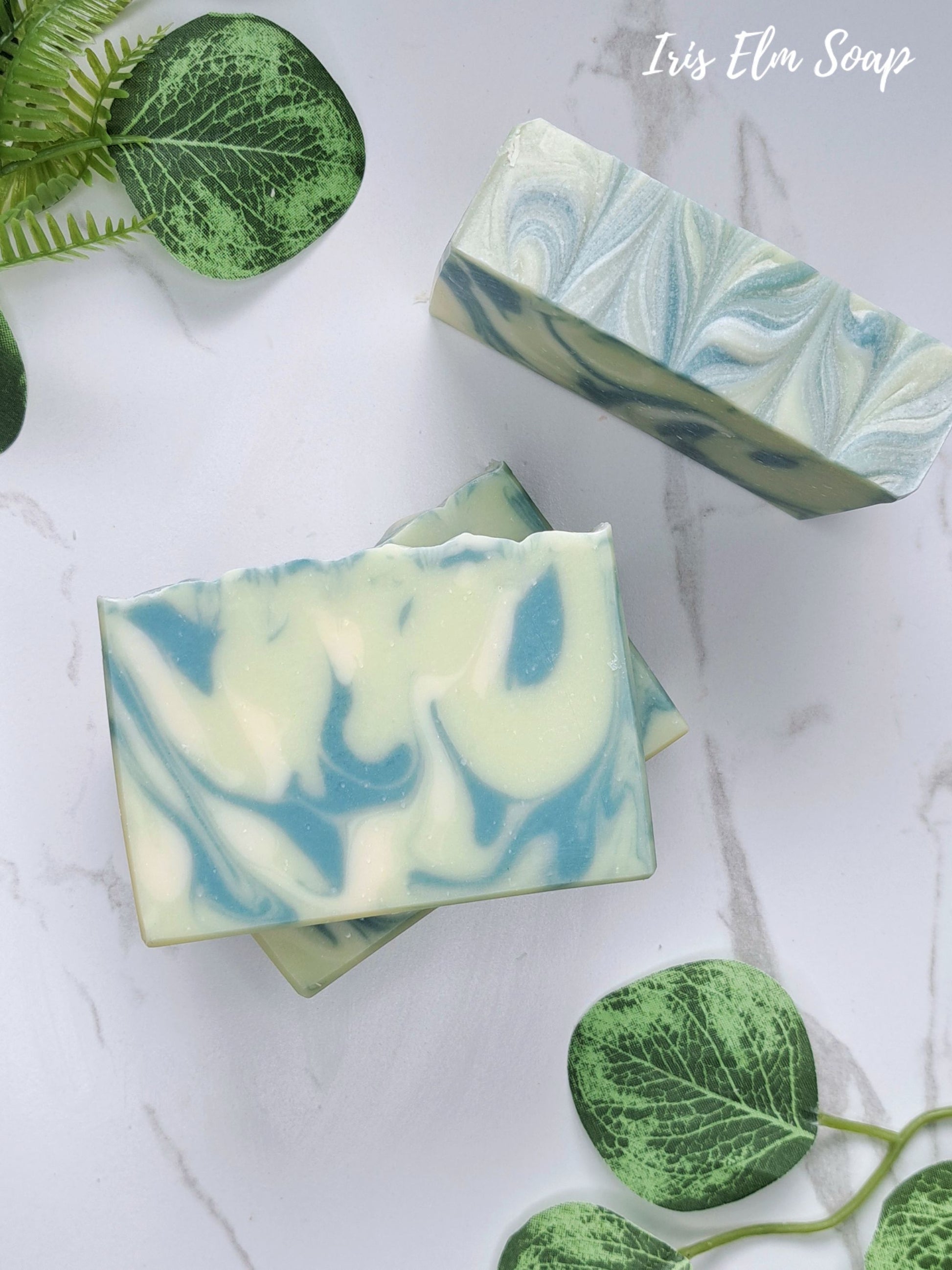 Three marbled agave lime handmade soap bars in green and white swirls, styled on a white marble surface with decorative green leaves. The text 'Iris Elm Soap' is visible in the top right corner.