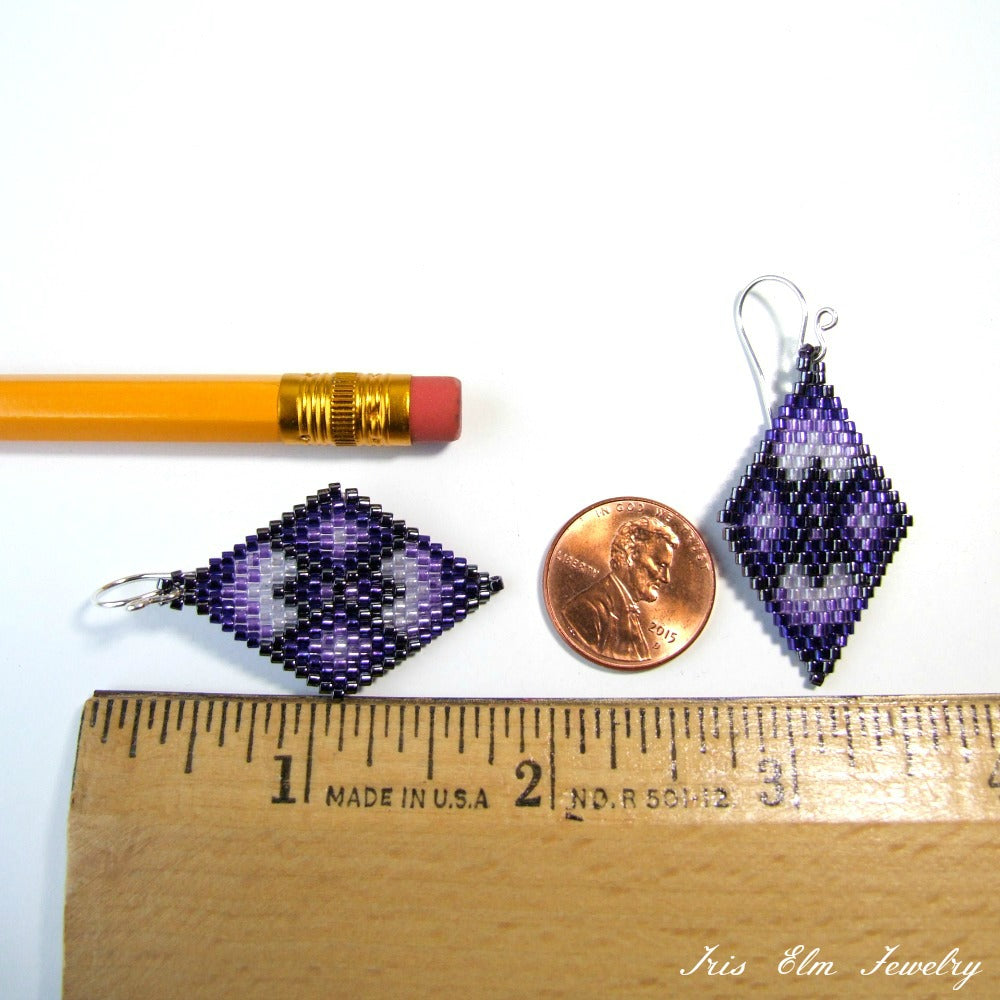 Two purple beaded earrings next to a penny and a ruler for scale on a white background.