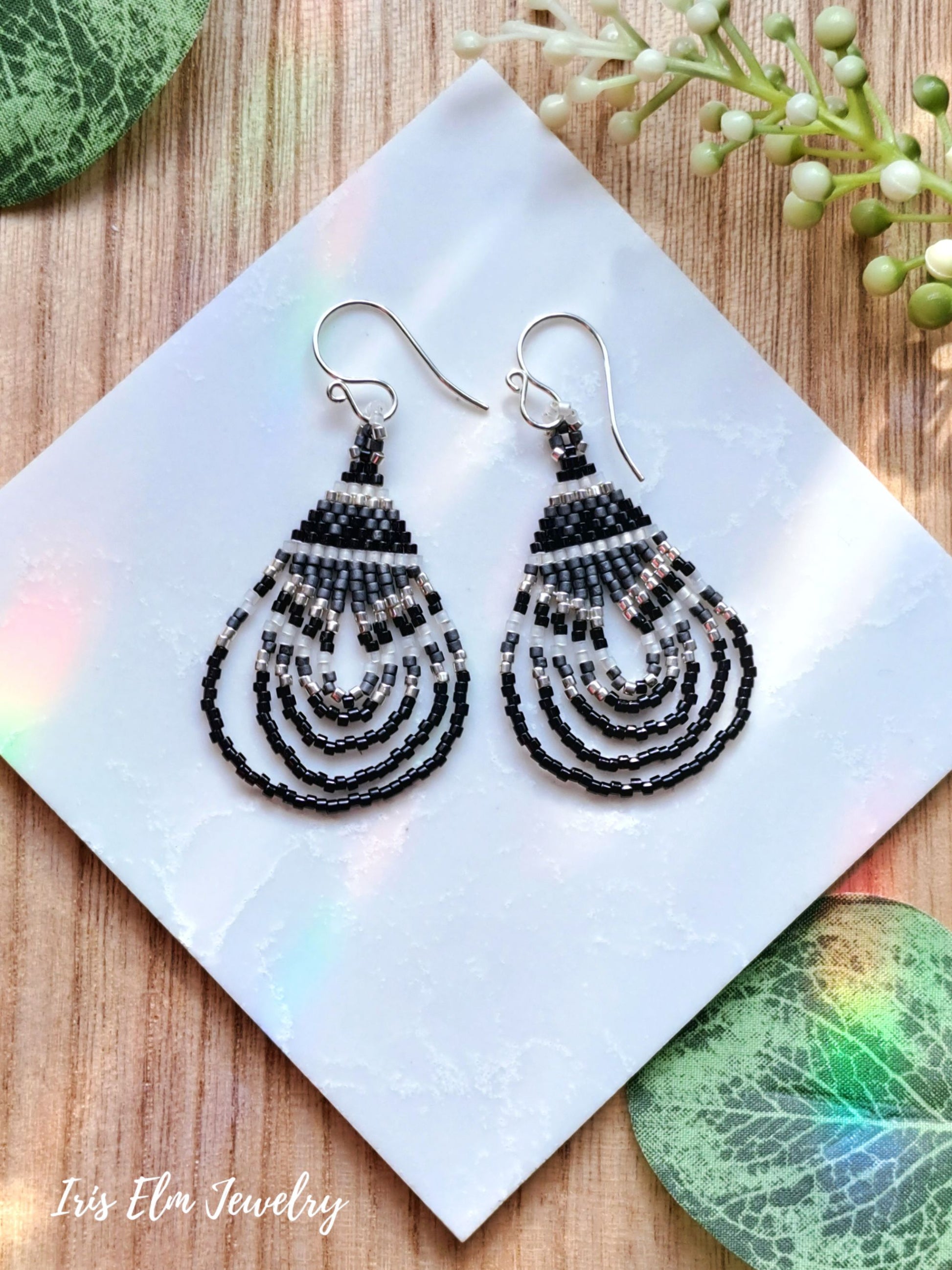 Black beaded seed bead teardrop earrings on a white card with green leaves in the background