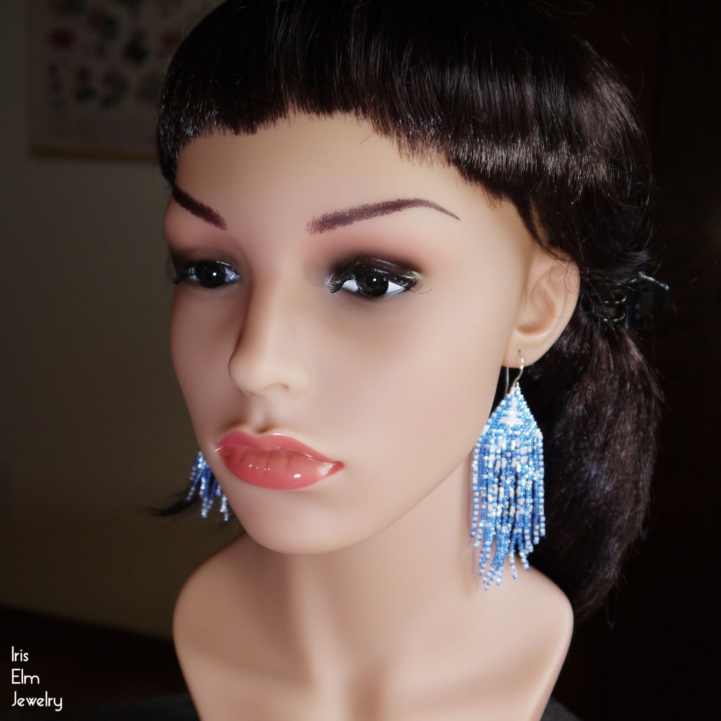 Mannequin head with blue beaded fringe earrings on a dark background
