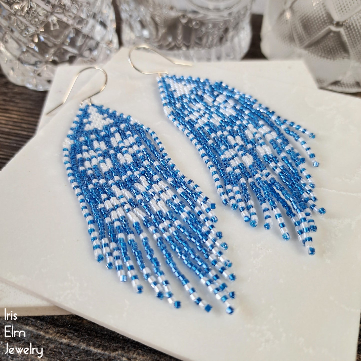 Blue and white beaded snowflake fringe handmade earrings on a white surface with 'Inis Elm Jewelry' branding.