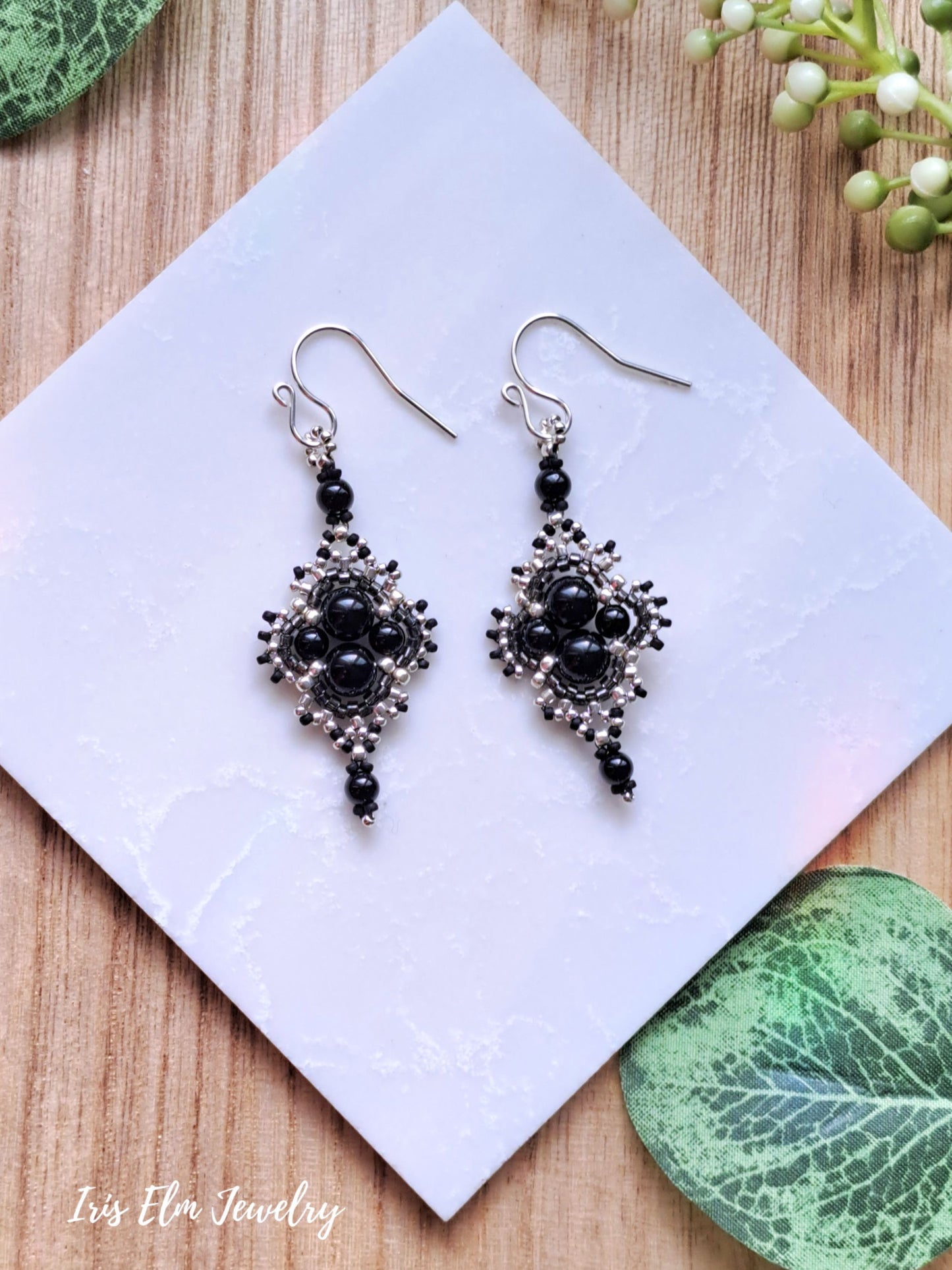 Black onyx beaded earrings on a white card with green leaves in the background