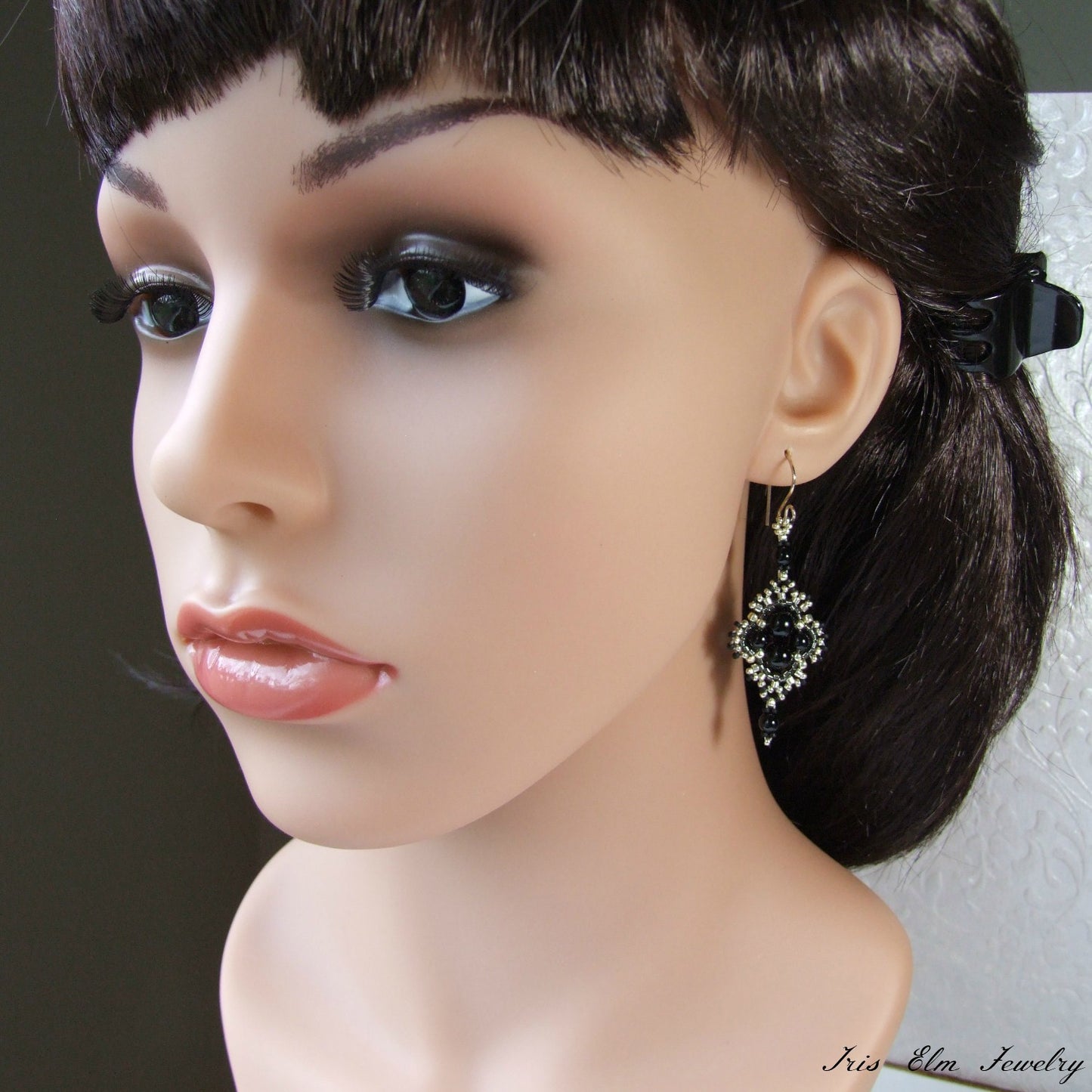 Mannequin head with black hair and a decorative black onyx earring on a neutral background