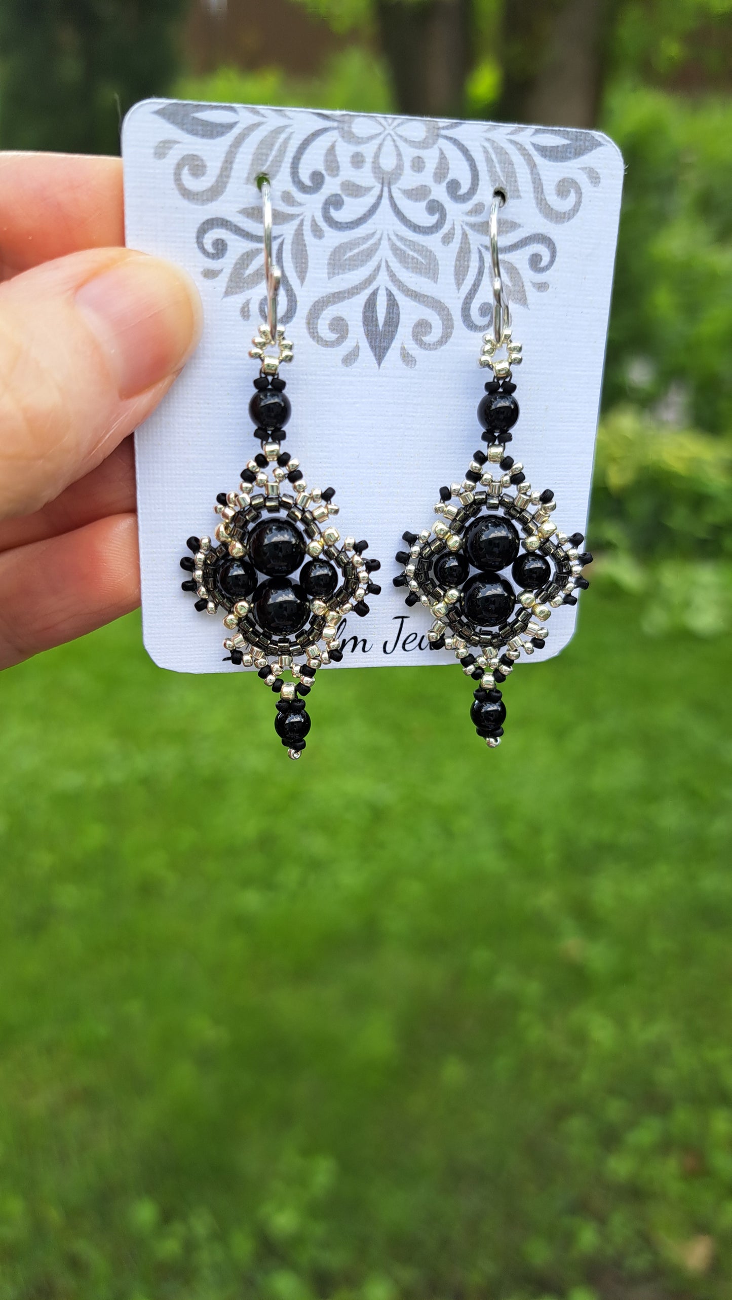 Black onyx beadwork earrings on a decorative card held by a hand with a green background