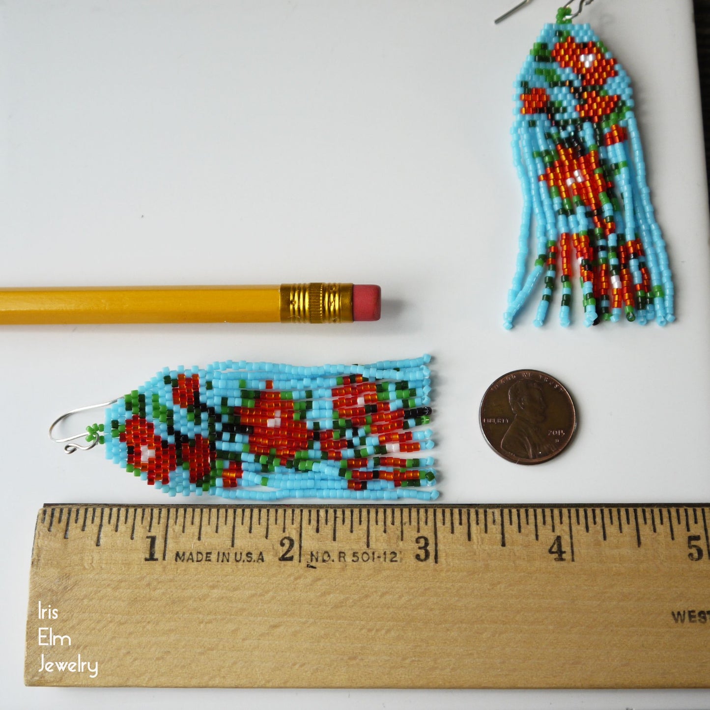 3 inch long beaded flower fringe earrings with a pencil and penny for scale, on a white background.
