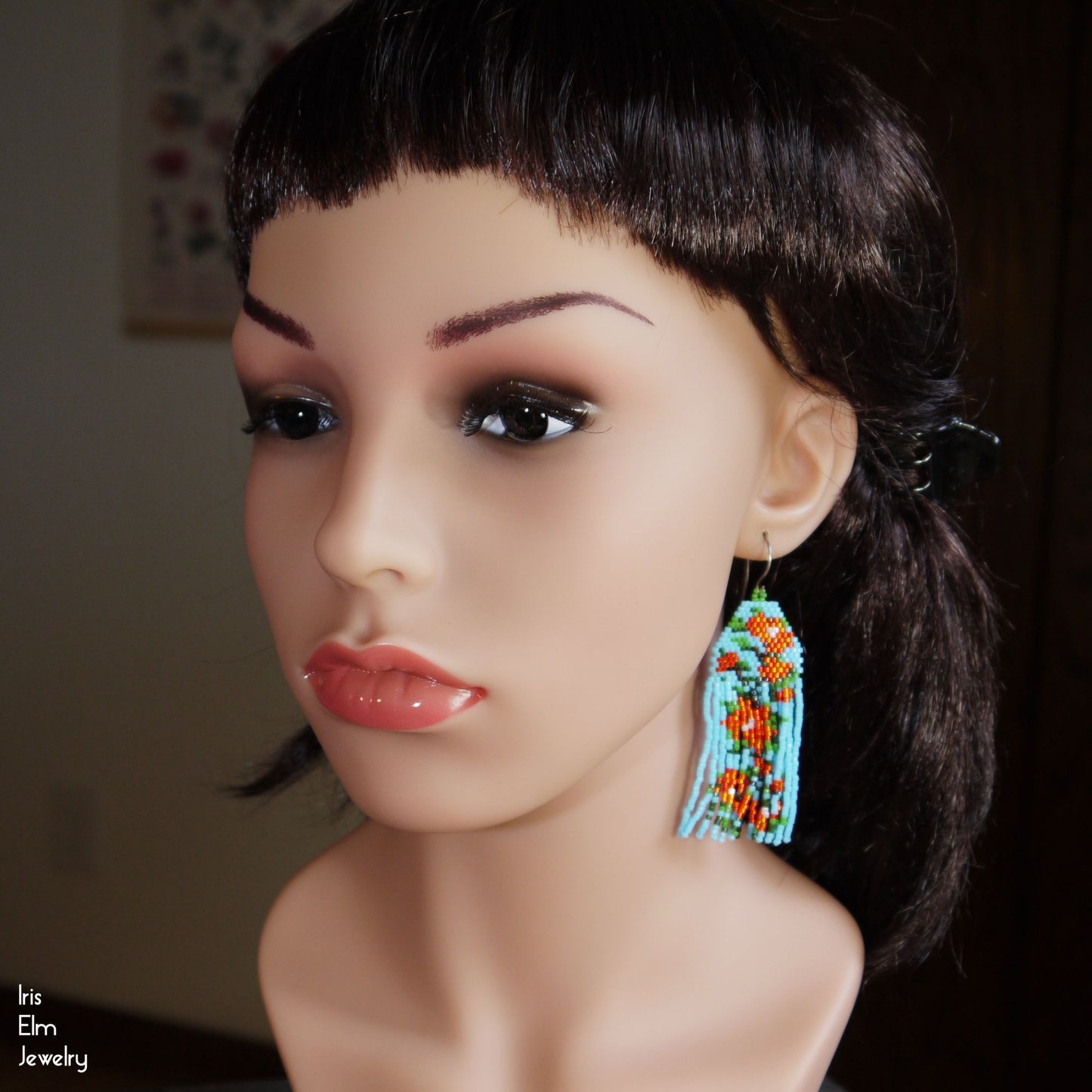 Mannequin head with colorful beaded flower fringe earrings on a blurred background