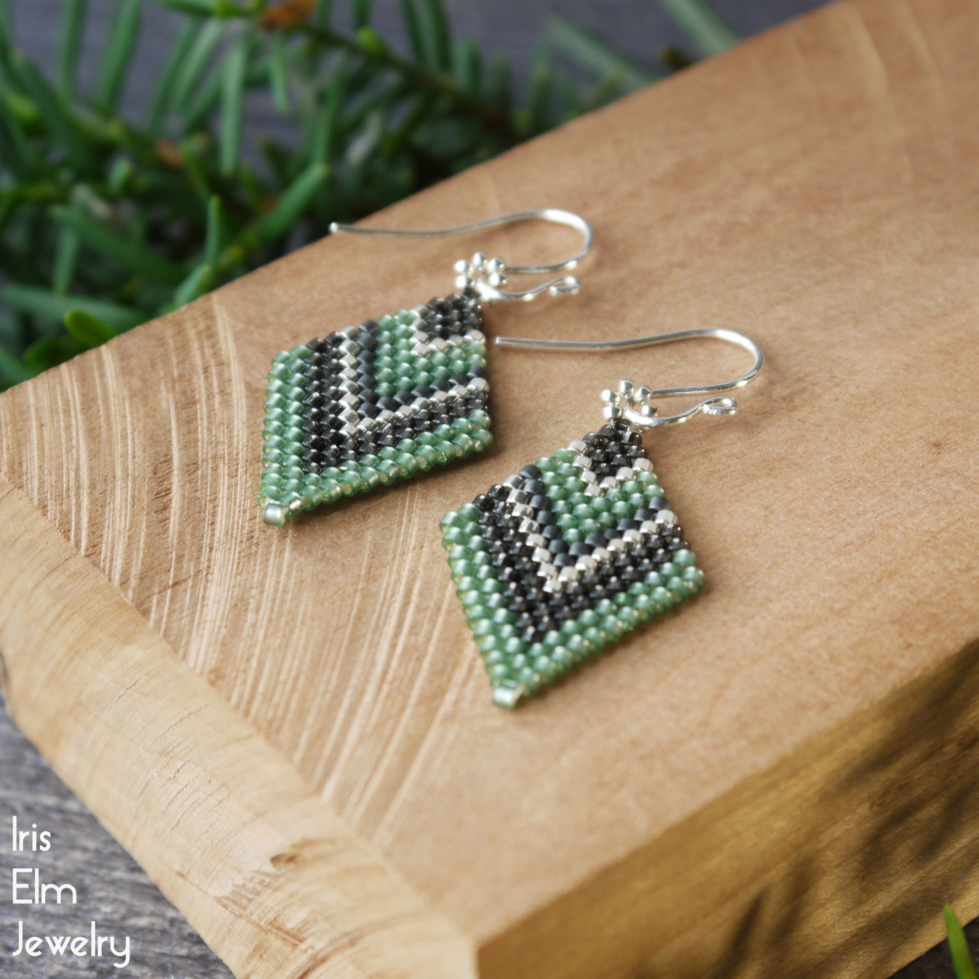 Green and dark grey handcrafted beadwork beaded earrings on a wooden surface with 'Iris Elm Jewelry' branding.