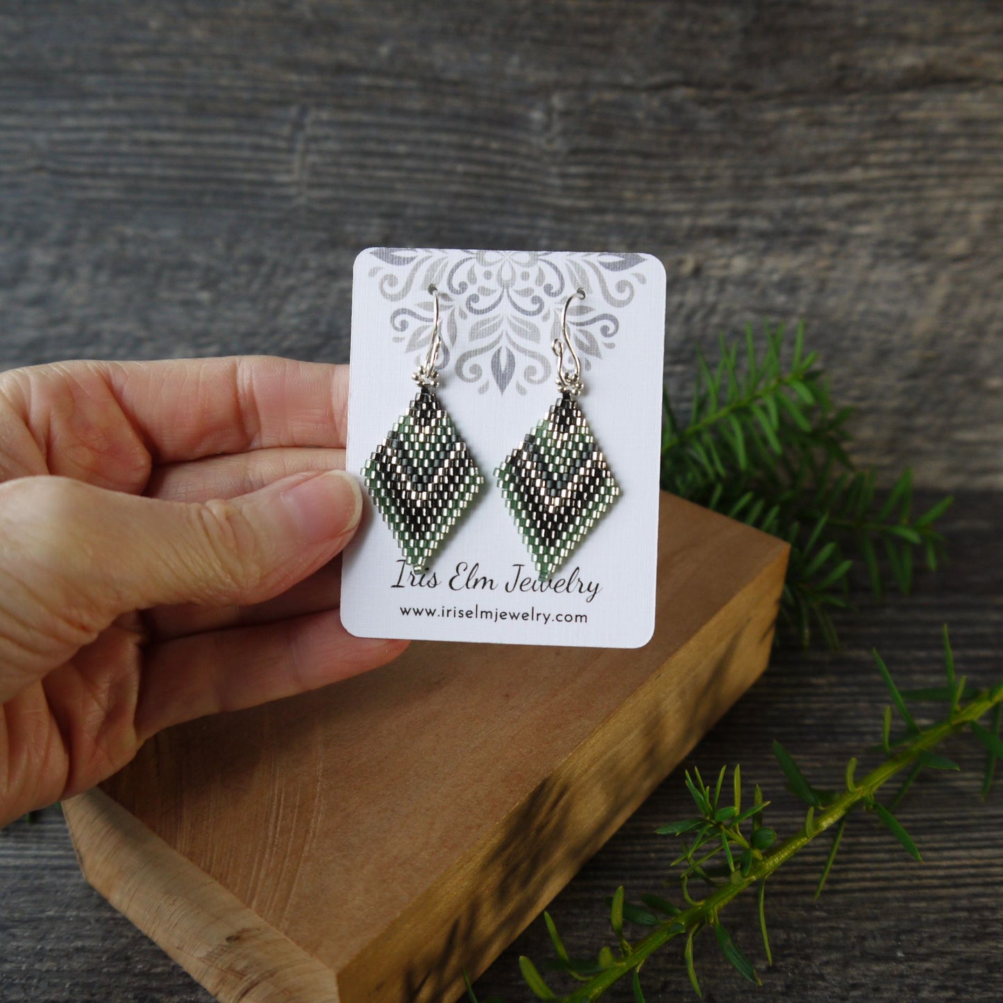 Hand holding a card with diamond-shaped earrings on a wooden block against a rustic background