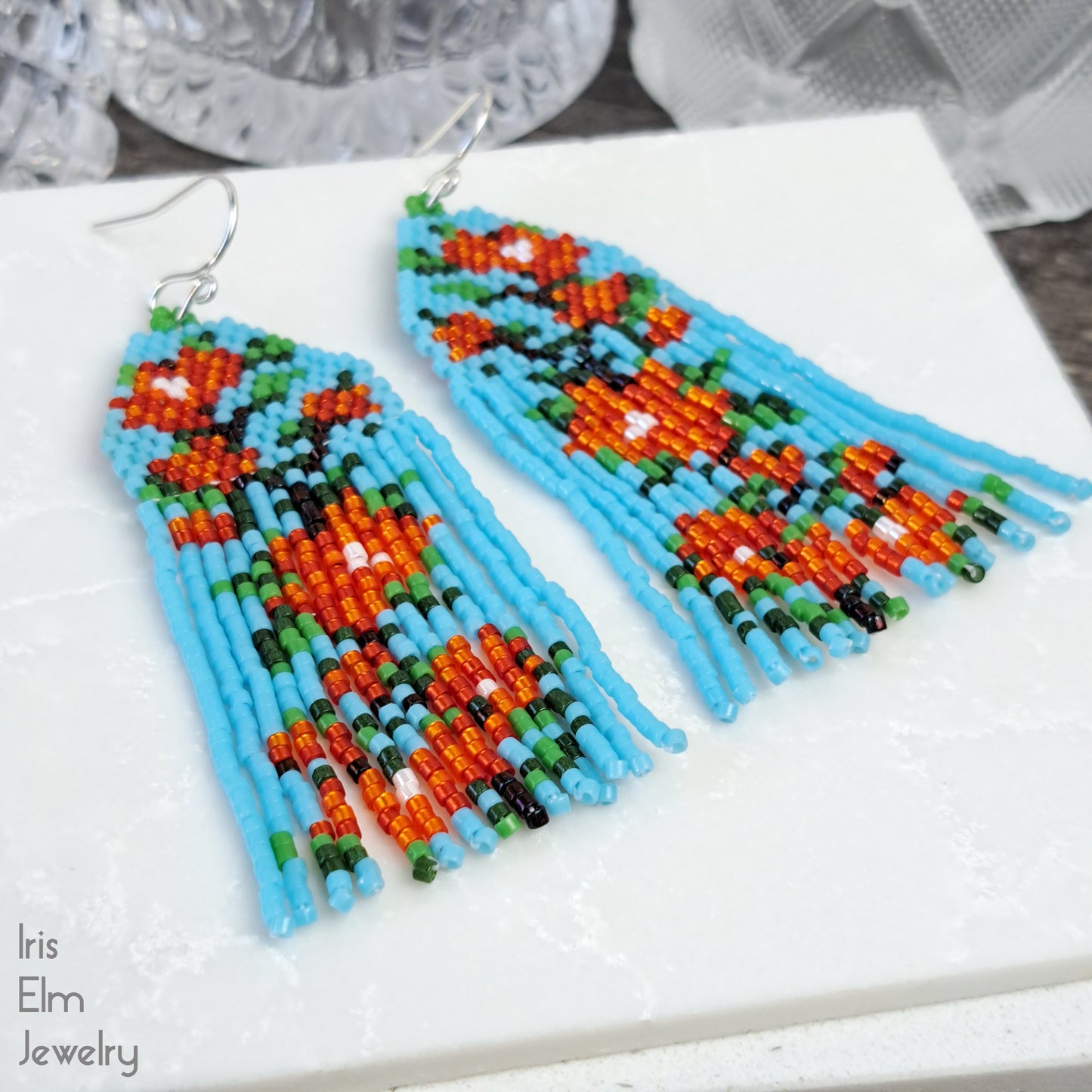 Colorful beaded floral fringe earrings on a white surface with 'Iris Elm Jewelry' branding.
