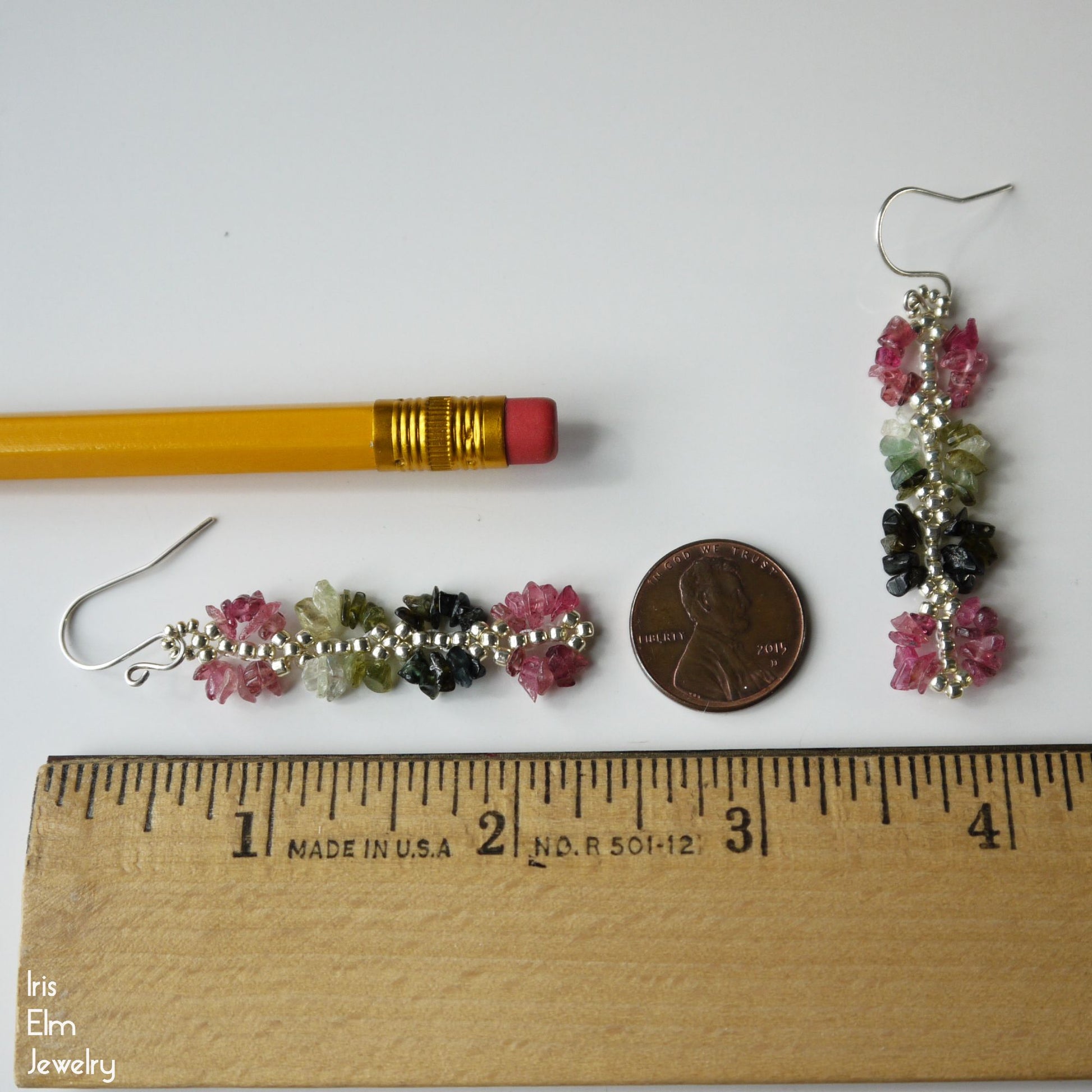 2 and 1/8 inch long rainbow tourmaline earrings with a pencil and penny for scale on a white background