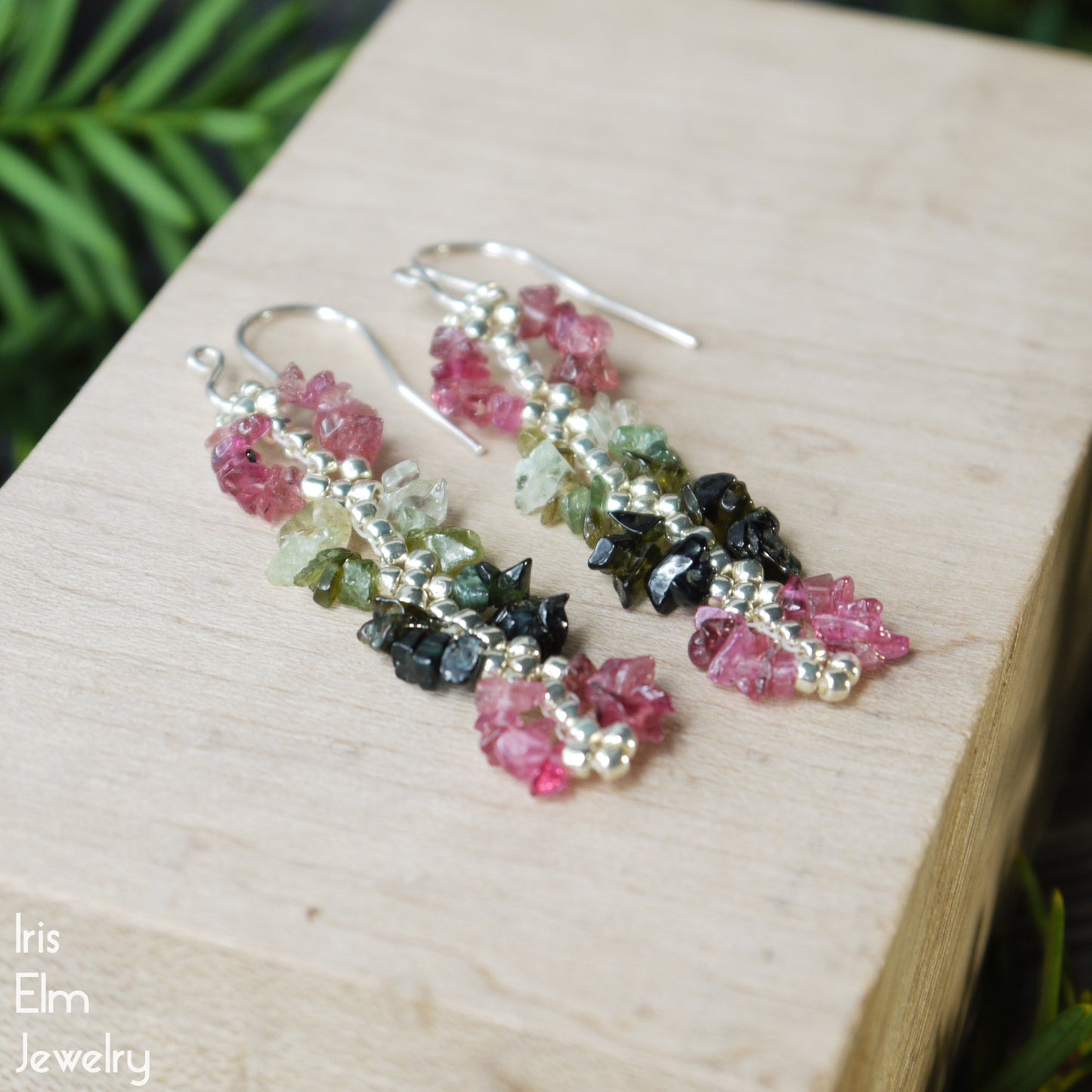 Multicolored gemstone pink and green rainbow tourmaline earrings on a wooden block with 'Iris Elm Jewelry' branding.