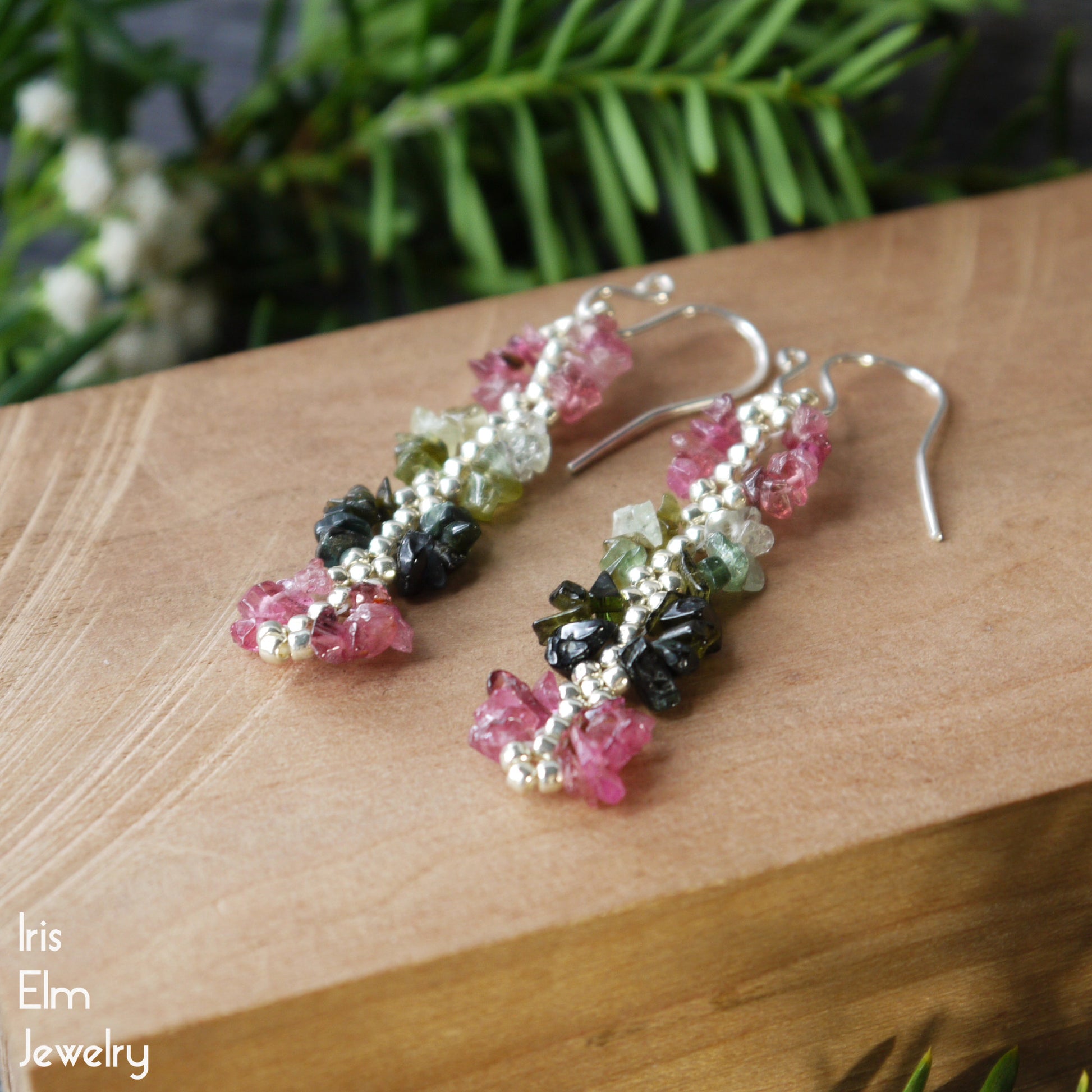 Colorful beaded pink and green rainbow tourmaline earrings on a wooden surface with 'Iris Elm Jewelry' branding.